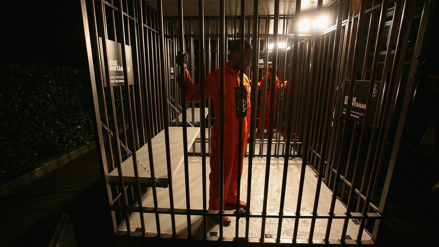 LONDON - JANUARY 10: Amnesty International supporters wearing orange boiler suits hold a night long vigil in a cage outside of the US embassy on January 10, 2008 in London, England. Amnesty International marks the six-year anniversary of the first prisoners being transported to Guantanamo Bay in Cuba. The human rights organisation installs its 'Guantanamo Cell' built to the exact dimensions of a cell at Guantanamo. (Photo by Daniel Berehulak/Getty Images)