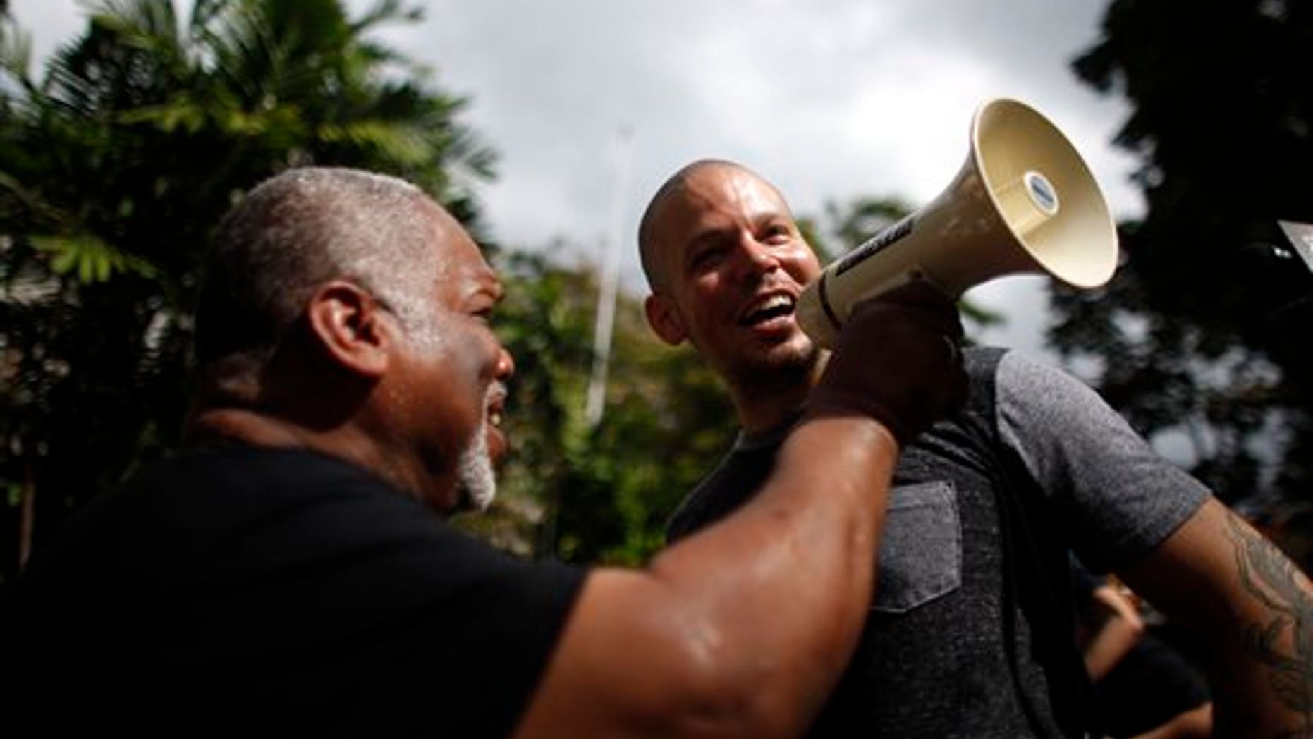 Striking teacher Jose Iturbe, left, holds up the megaphone to entertainer Rene Perez Joglar, also known as "Residente" from Puerto Rico's musical group Calle 13, who joined the protest by striking teachers outside a public school in San Juan, Puerto Rico, Tuesday, Jan. 14, 2014. Hundreds of teachers across Puerto Rico walked off their jobs in a two-day strike over cuts to their pensions that the island's government says are necessary to avert financial disaster but that educators say will force many of them into poverty. (AP Photo/Ricardo Arduengo)