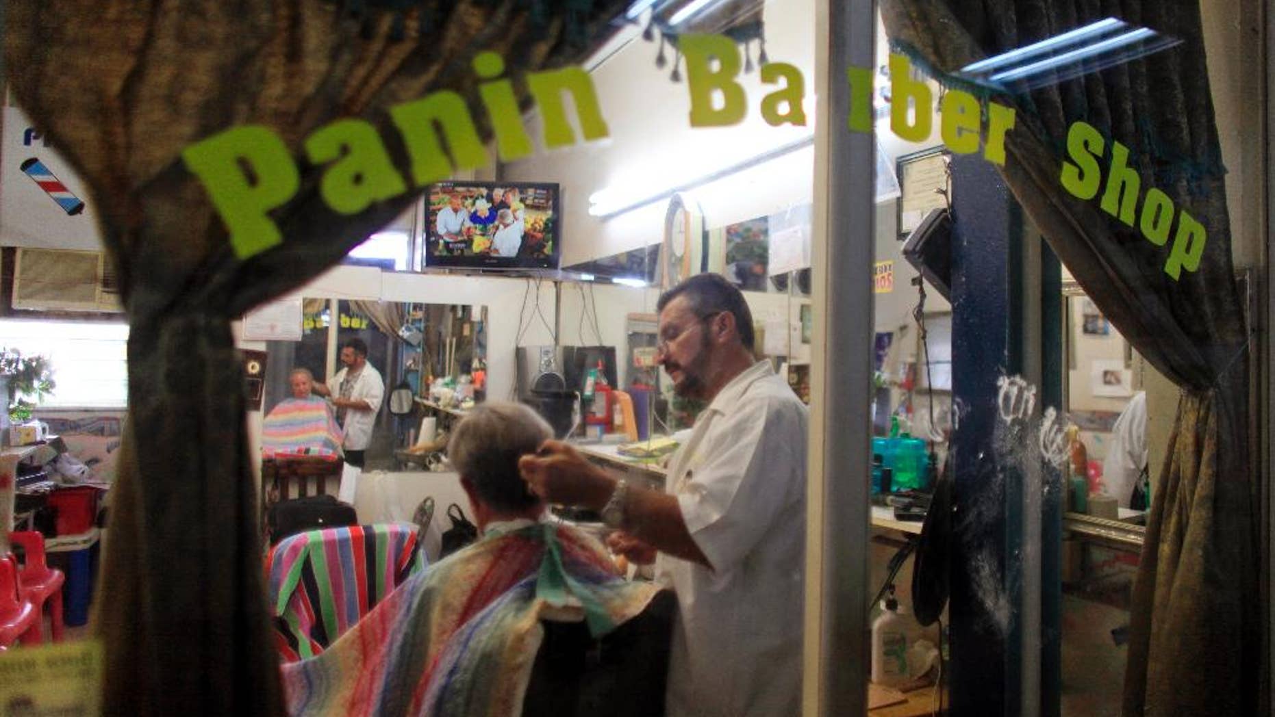 In this Sept. 2, 2015 photo, Francisco Gonzalez gives a haircut to a customer at his barbershop in Lares, Puerto Rico. Despite the economic downturn, some business owners are determined to stick it out in Lares. (AP Photo/Ricardo Arduengo)