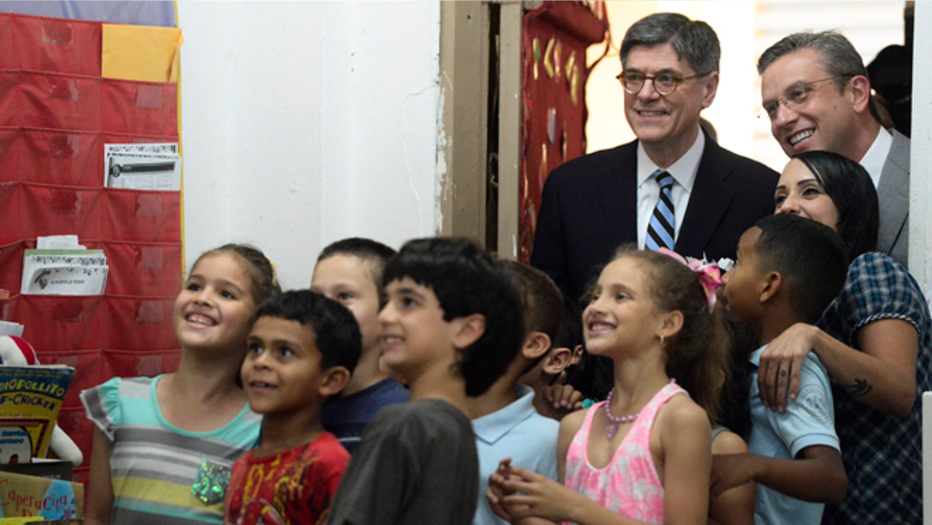 U.S. Treasury Secretary Jacob Lew, top, second from right, poses for photos with students as he takes a classroom tour with Puerto Rico Governor Alejandro Garcia Padilla, top right, at the Eleanor Roosevelt Elementary School in San Juan, Puerto Rico, Monday, May 9, 2016. Lew hoped to jump-start congressional efforts to aid debt-stricken Puerto Rico, traveling to the U.S. territory on Monday and focusing on basic services in jeopardy at public hospitals and schools. (AP Photo/Carlos Giusti)