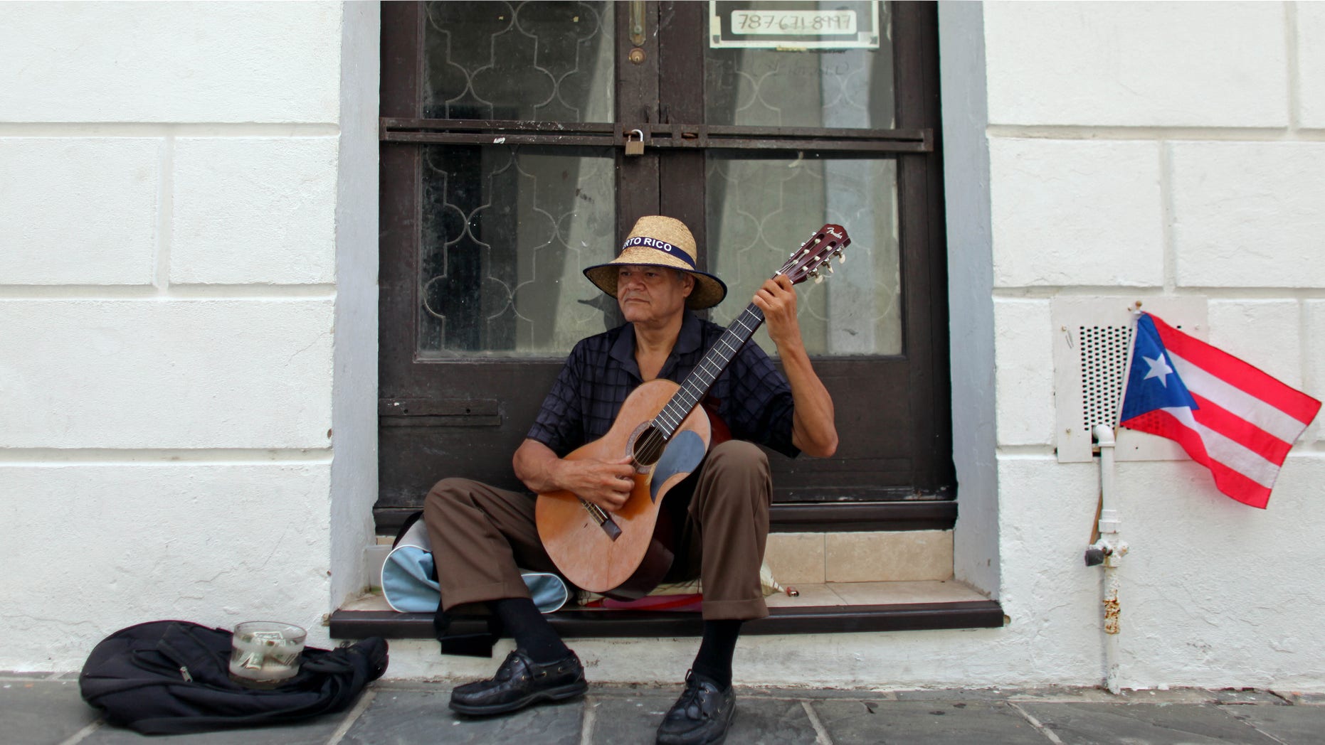 A man plays his guitar while he begs for money in front of a closed down business in Old San Juan, Puerto Rico, Monday, June 29, 2015. International economists released a critical report on Puerto Rico's economy Monday on the heels of the governor's warning that the island can't pay its $72 billion public debt. (AP Photo/Ricardo Arduengo)