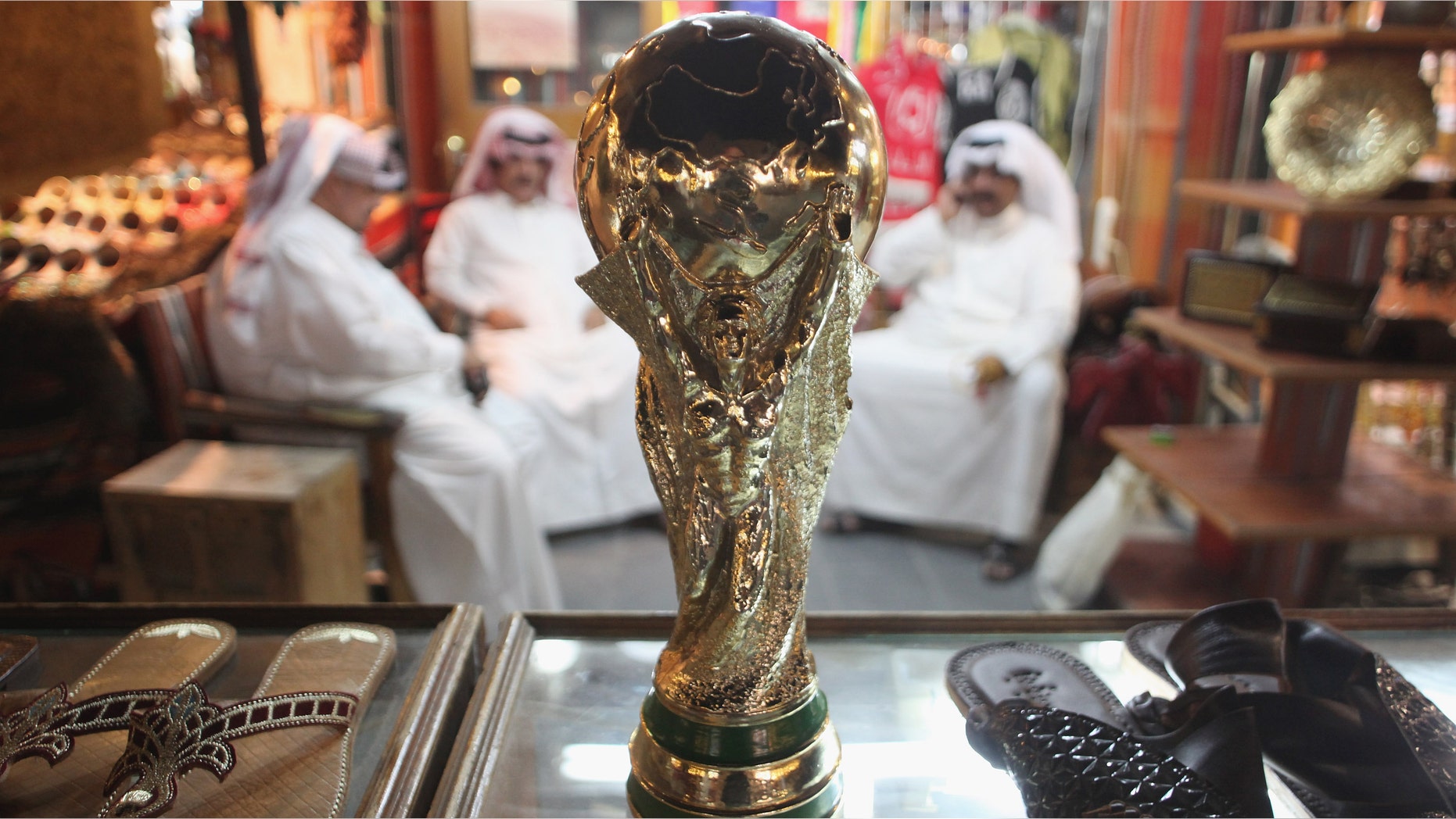 DOHA, QATAR - OCTOBER 24: Arab men sit at a shoemaker's stall with a replica of the FIFA World Cup trophy in the Souq Waqif traditional market on October 24, 2011 in Doha, Qatar. Qatar will host the 2022 FIFA World Cup football competition and is slated to tackle a variety of infrastructure projects, including the construction of new stadiums. (Photo by Sean Gallup/Getty Images)