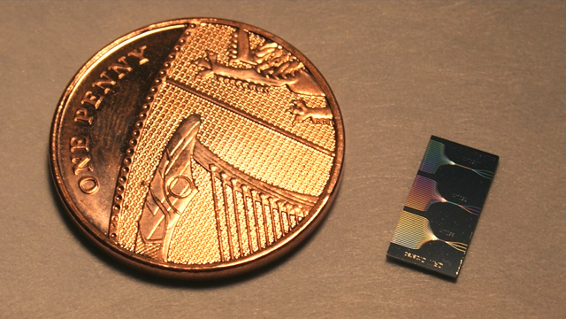 This is the photonic chip next to a UK penny. The chip contains micrometer and sub-micrometer features and guide light using a network of waveguides. The output of this network can be seen on the surface of the chip.