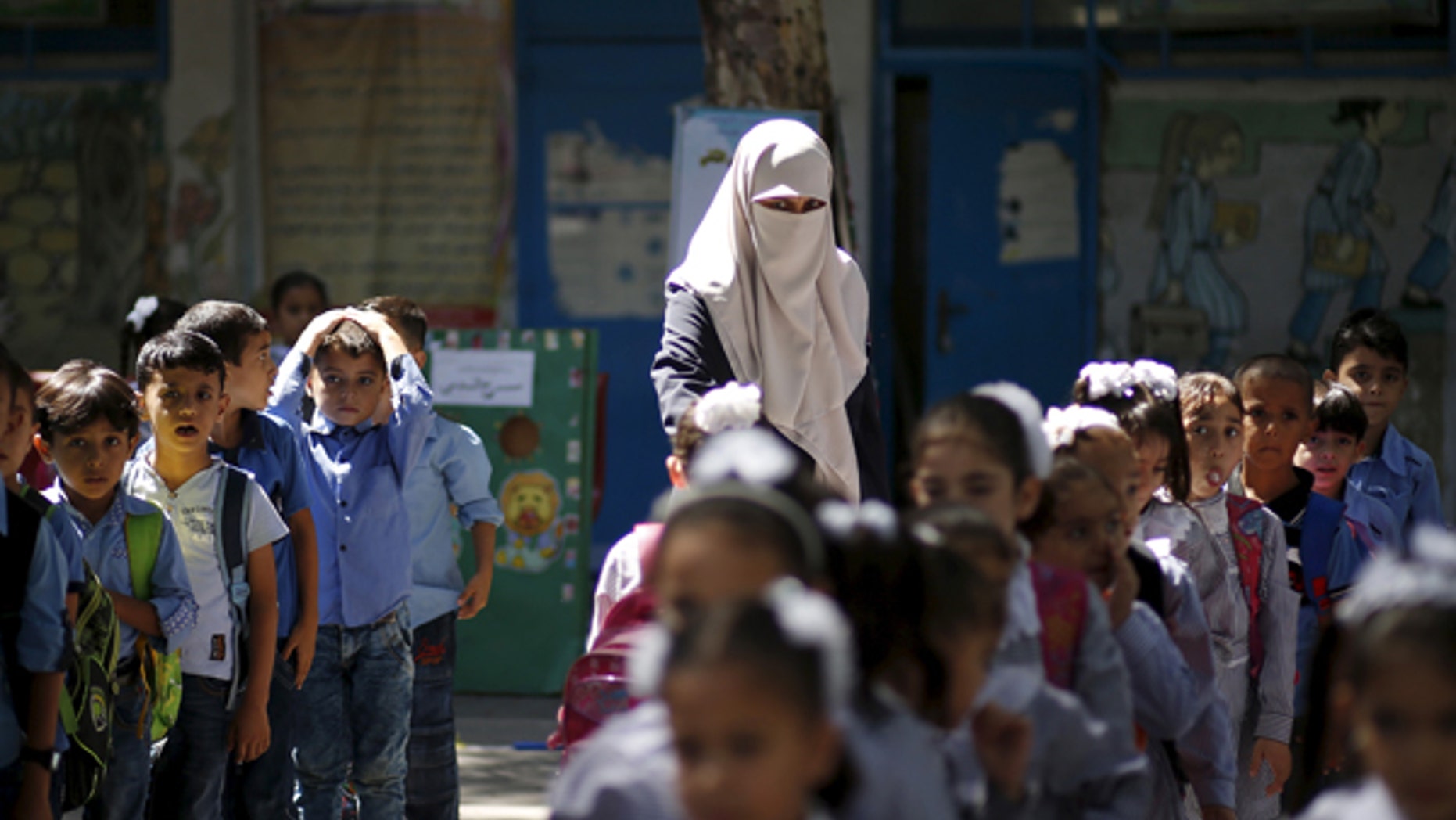September 22, 2015: A veiled Palestinian teacher stands next to children as they queue at a United Nations Relief and Work Agency (UNRWA)-run school in Gaza. A recent investigation by the Center for Near East Policy Research found that many of the schools are using texts that are authored by the Palestinian Ministry of Education and its contents not fail to recognize the state of Israel.