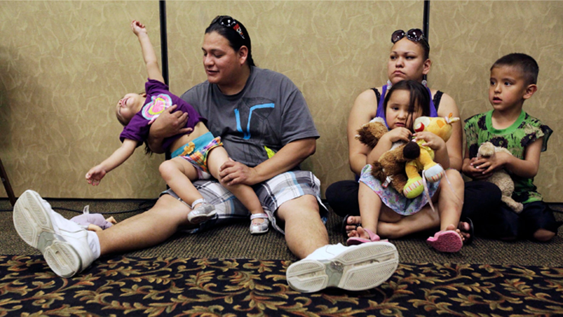 FILE - In this Wednesday, May 15, 2013 file photo, Elijah Bearsheart, left, holds his daughter, Keanala, 1, as he sits with his family, Kehala Diserly, Kiari Diserly, 3, and Yamni Pederson, 5, as they listen to testimony during the Indian Child Welfare Act summit in Rapid City, S.D. A new report on child well-being, measured by state and race, has turned an unflattering spotlight on some places not used to being at the bottom of such lists, including Wisconsin, with a worst-in-the-nation ranking for its black children, and South Dakota, with abysmal results for its American Indian youth. The report was released Tuesday, April 1, 2014 by the Annie E. Casey Foundation. (AP Photo/Rapid City Journal, Benjamin Brayfield)