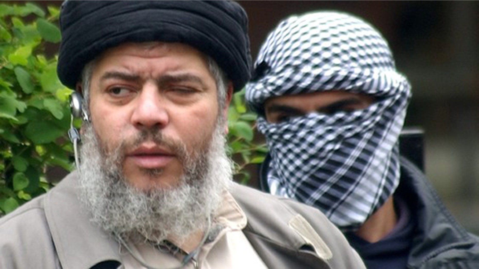 FILE 2004: Abu Hamza al-Masri arrives with a masked bodyguard to conduct prayers in the street outside the closed Finsbury Park Mosque in London
