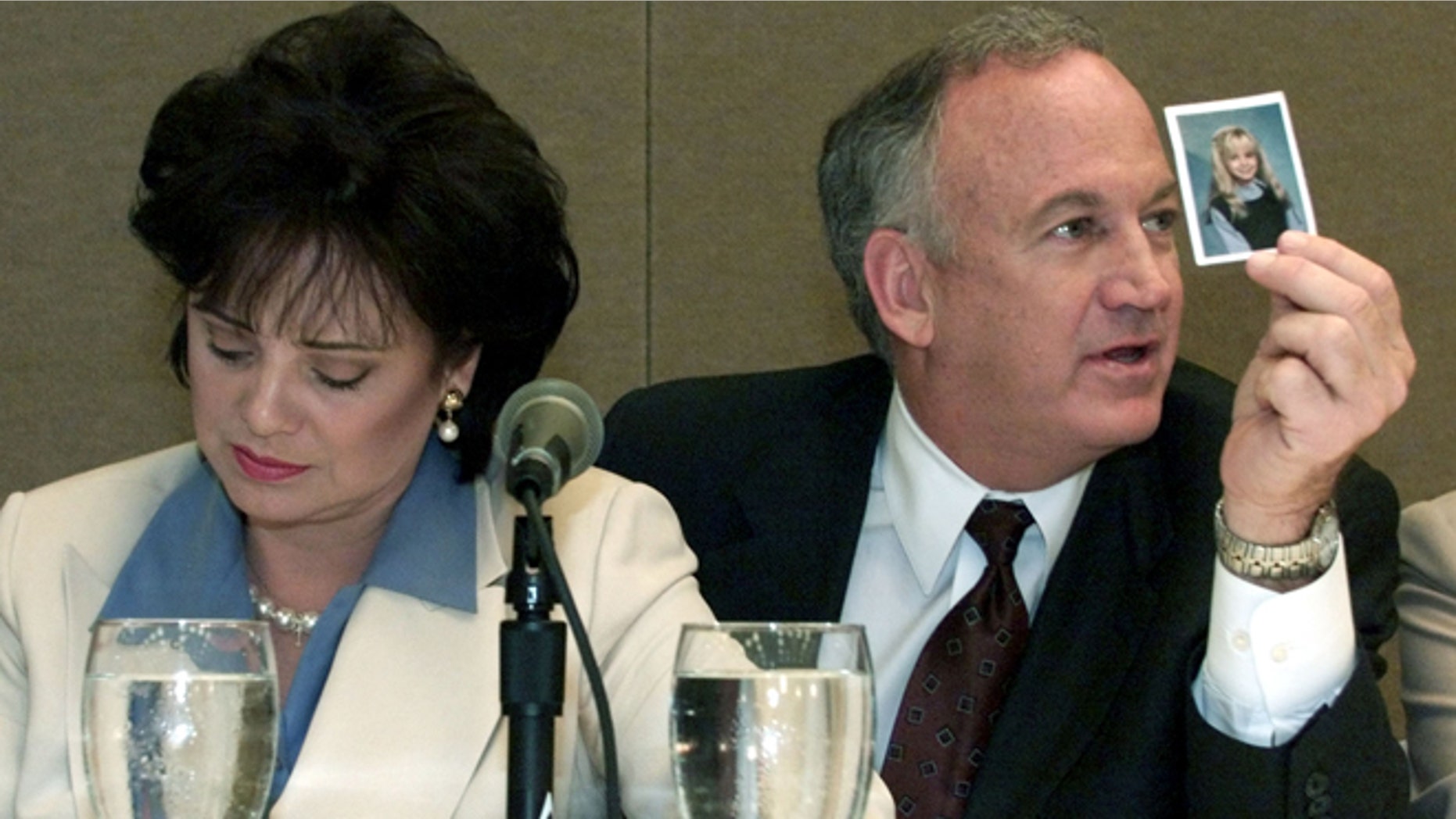 Patsy Ramsey looks down as her husband John Ramsey (R) produces a picture of Jon-Benet Ramsey during a press conference in Atlanta where they released the results of an independant lie detector test on May 24. The Ramsey's appeared with their attorneys and the officials who administered the test stating that they had no knowledge of who killed their daughter Jon-Benet Ramsey in Boulder,Colorado.TLC/RCS - RTR4MMH