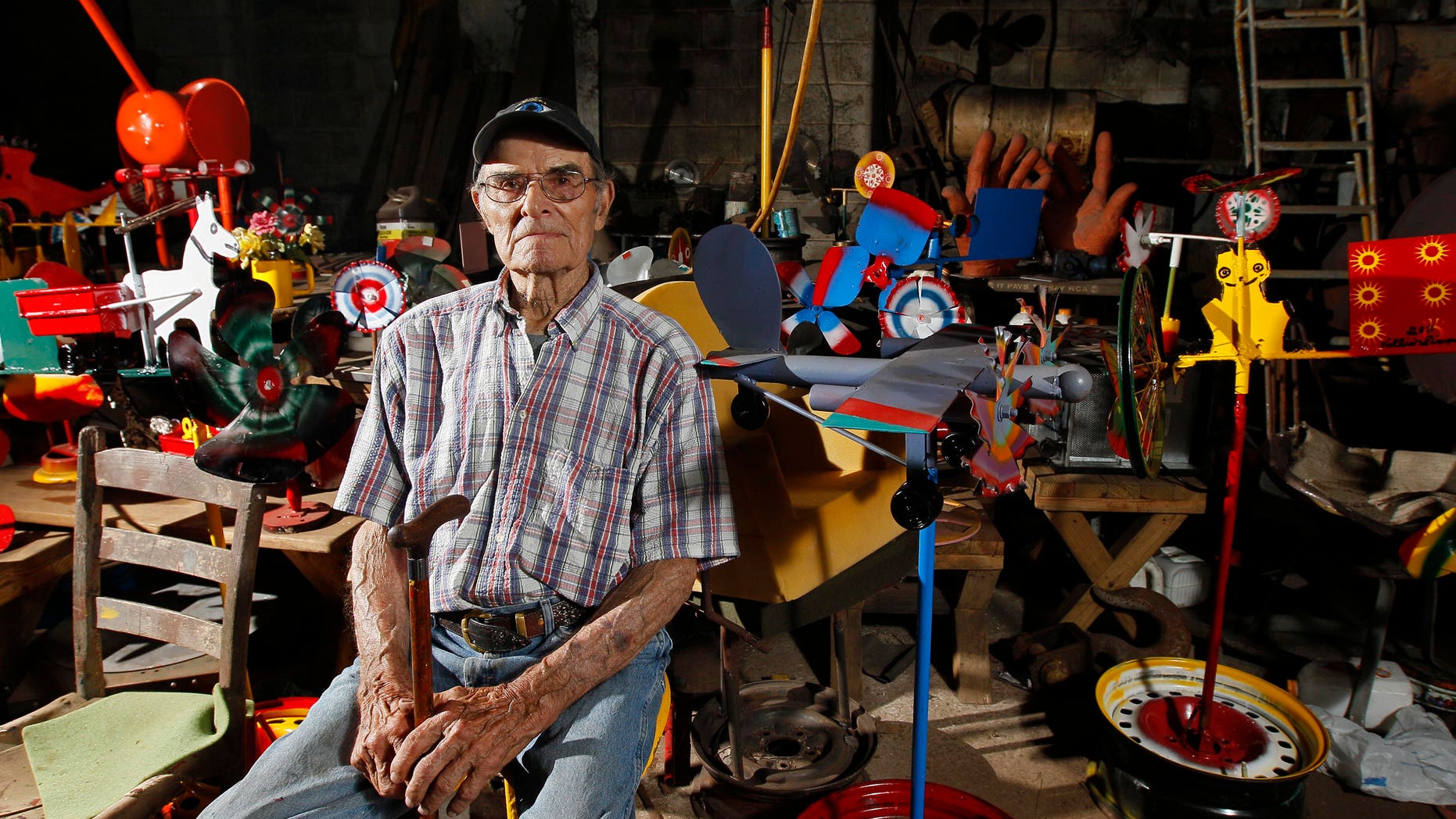 In this photo taken Thursday, June 21, 2012, whirligig artist Vollis Simpson sits in his shop surrounded by his whirligigs in Lucama, N.C., Thursday, June 21, 2012. In a huge warehouse a few miles from where Simpson's whirligigs have stood for years, people spend their days repairing the wind-driven creations, giving them the same attention that one gives a Picasso. They're repairing the whirligigs in advance of moving them next year to a downtown park. (AP Photo/Gerry Broome)