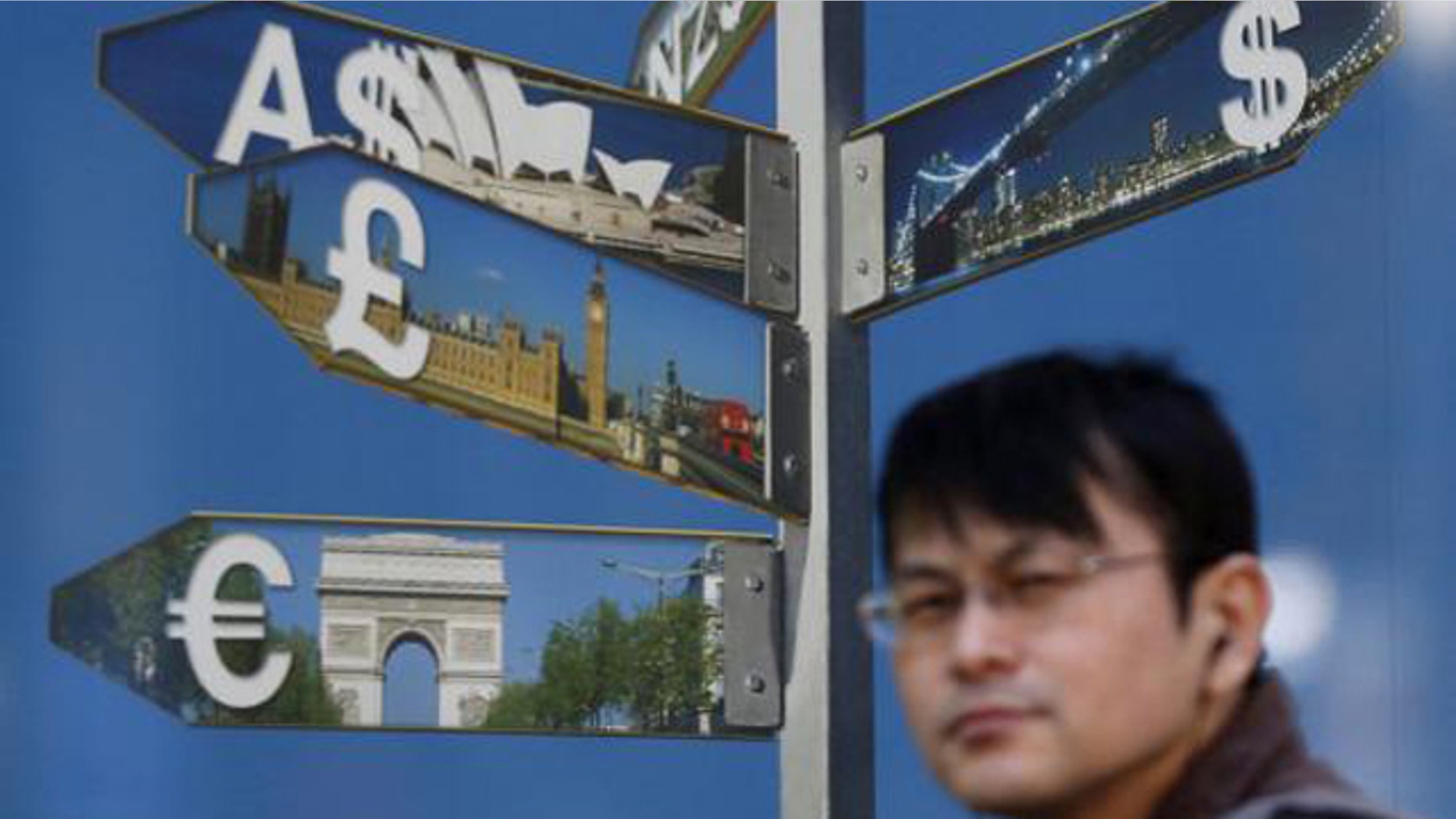 October 28, 2014: A man walks past various currency signs, including the dollar, Australian dollar, pound sterling and euro, outside a brokerage in Tokyo (Reuters/Yuya Shino)