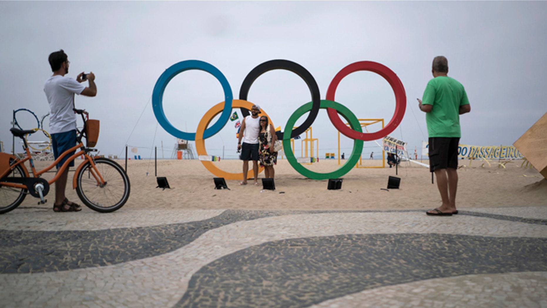 In this July 25, 2016 photo, people take photos by the Olympic rings decorating Copabana Beach in Rio de Janeiro, Brazil. In the city's 2009 Olympic bid document, authorities pledged the games would 'regenerate Rio's magnificent waterways.' A promised billion-dollar investment in cleanup programs was meant to be among the games' most important legacies, but once more, the lofty promises have ended in failure. (AP Photo/Felipe Dana)