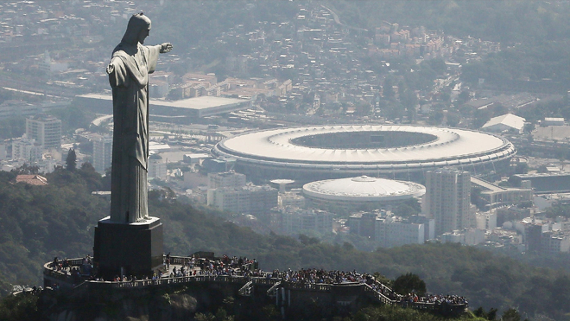 RIO DE JANEIRO, BRAZIL - JULY 04: Visitors gather beneath the Christ the Redeemer statue as Maracana stadium, site of the Olympic opening ceremonies, stands in the background on July 4, 2016 in Rio de Janeiro, Brazil. July 5 marks the one-month mark to the beginning of the Rio 2016 Olympic Games with an economic crisis, political turmoil and Zika virus fears roiling the country. (Photo by Mario Tama/Getty Images)