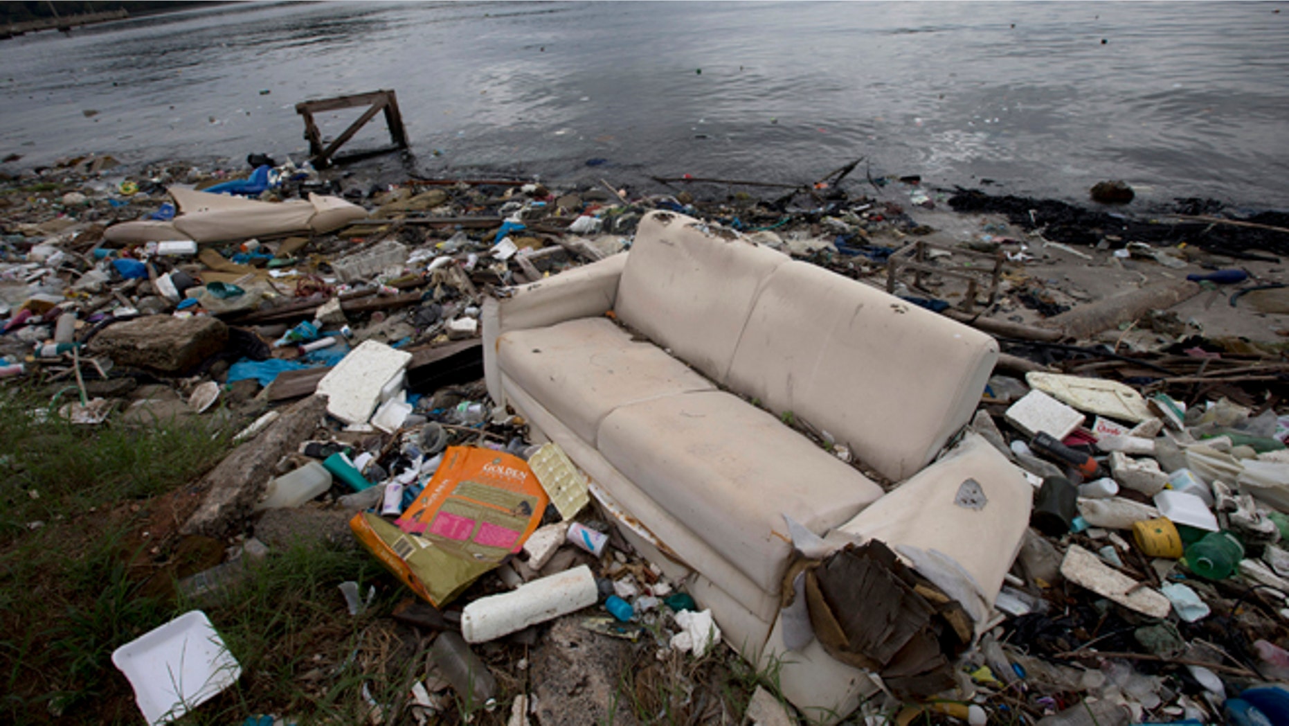 In this June 1, 2015 file photo, a discarded sofa litters the shore of Guanabara Bay in Rio de Janeiro, Brazil. As part of its Olympic bid, Brazil promised to build eight treatment facilities to filter out much of the sewage and prevent tons of household trash from flowing into the Guanabara Bay. Only one has been built. Tons of household trash line the coastline and form islands of refuse. (AP Photo/Silvia Izquierdo, File)