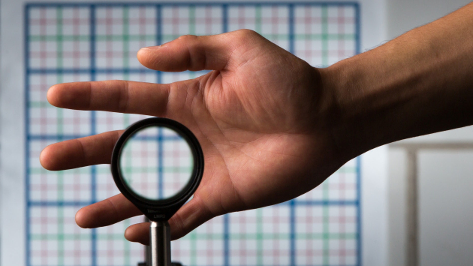 A multidirectional `perfect paraxial' cloak using 4 lenses. For a continuous range of viewing angles, the hand remains cloaked, and the grids seen through the device match the background on the wall (about 2 m away), in color, spacing, shifts, and magnification. The edges of the optics can be seen since this is a small-angle ('paraxial') cloak, but this can be reduced by using large optics and for distant viewing; also the center of the device must not be blocked. // an optical cloaking configuration designed by University of Rochester professor of physics John C. Howell and Ph.D. student Joseph Choi is pictured in Bausch & Lomb Hall September 11, 2014. // photo by J. Adam Fenster / University of Rochester