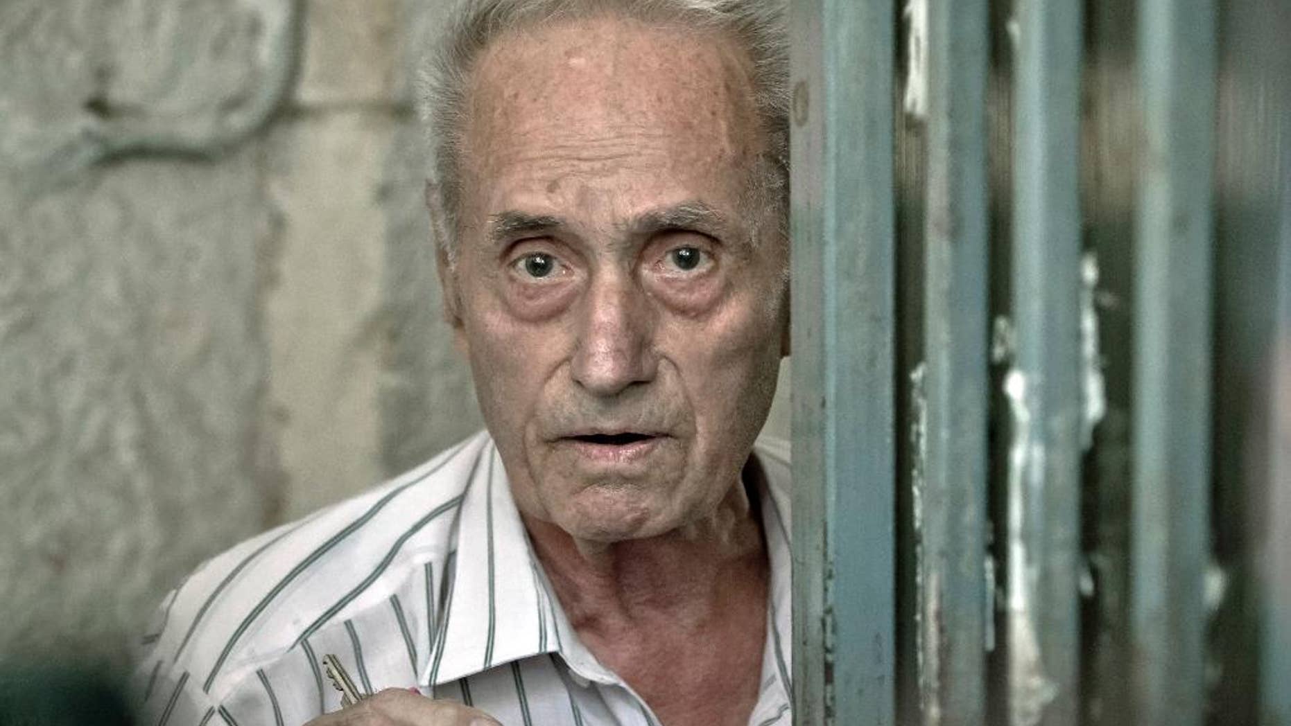 FILE - This is a Tuesday, July 30, 2013 file photo of retired Lt. Col. Alexandru Visinescu, 87, looks at journalists outside his home in Bucharest, Romania. A court on Wednesday Oct. 22, 2014 froze the assets of a former Romanian prison commander Alexandru Visinescu, charged with torturing and causing the deaths of 12 political prisoners in the 1950s and 1960s and said the government may also be liable to pay damages to alleged victims. (AP Photo/Vadim Ghirda, File)