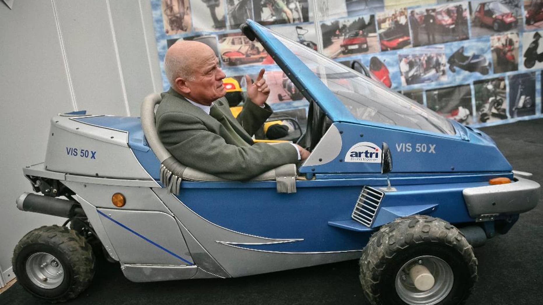 In a photo taken on March 24, 2009, Justin Capra, a Romanian inventor who claimed he beat the Americans to make the world’s first jet-pack, seen on photo wall behind top left, gestures sitting in a fuel efficient vehicle he designed at an inventions fair in Cluj, Romania. Capra, who in 1956 invented the “flying rucksack,” a personal flying machine, very similar, according to him to the one built in 1962 in the U.S. by Bell Aircraft Corp., has died Monday, Jan. 19, 2015, aged 81.(AP Photo/Mircea Rosca)