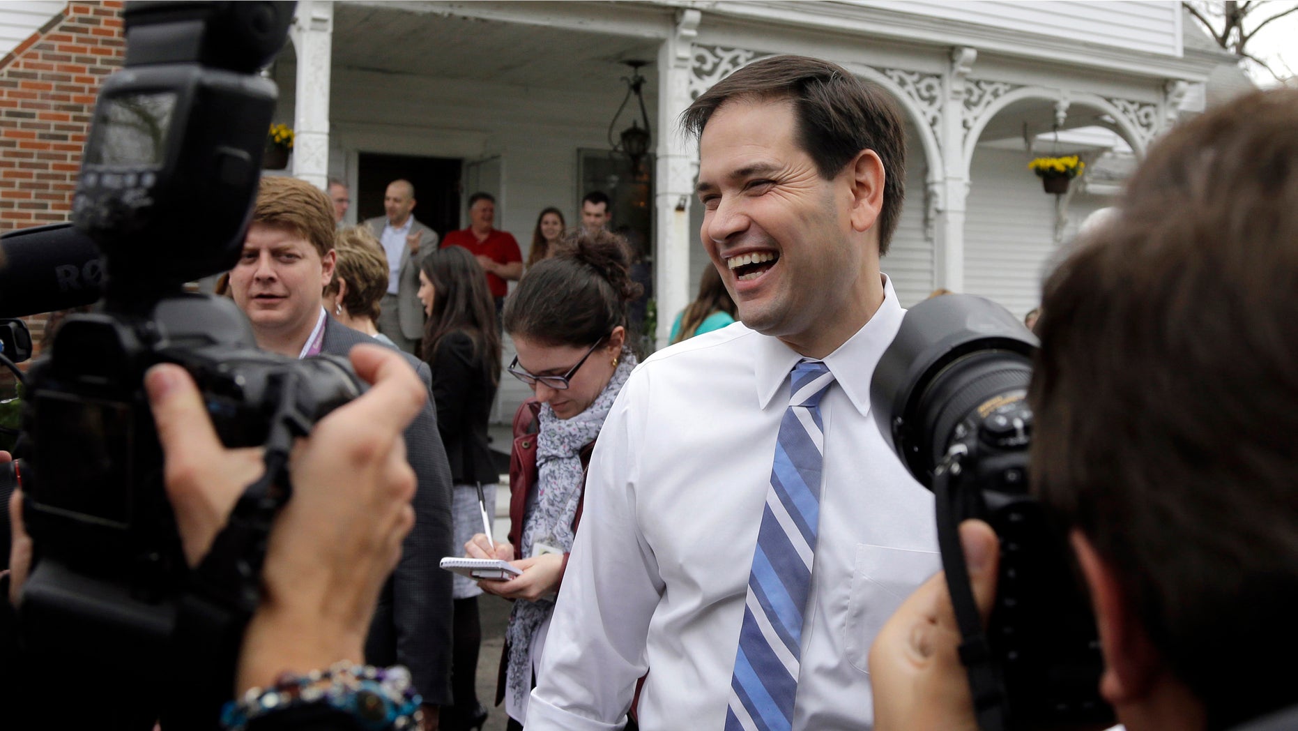 In this April 17, 2015 photo, Republican presidential candidate, Sen. Marco Rubio, R-Fla., laughs as he is surrounded by media at a campaign house party in Manchester, N.H. Devoted political allies for more than a decade, the alliance between former Florida Gov. Jeb Bush and Rubio is beginning to splinter as the one-time mentor and his political protégé face off in the race for the Republican presidential nomination. (AP Photo/Elise Amendola)