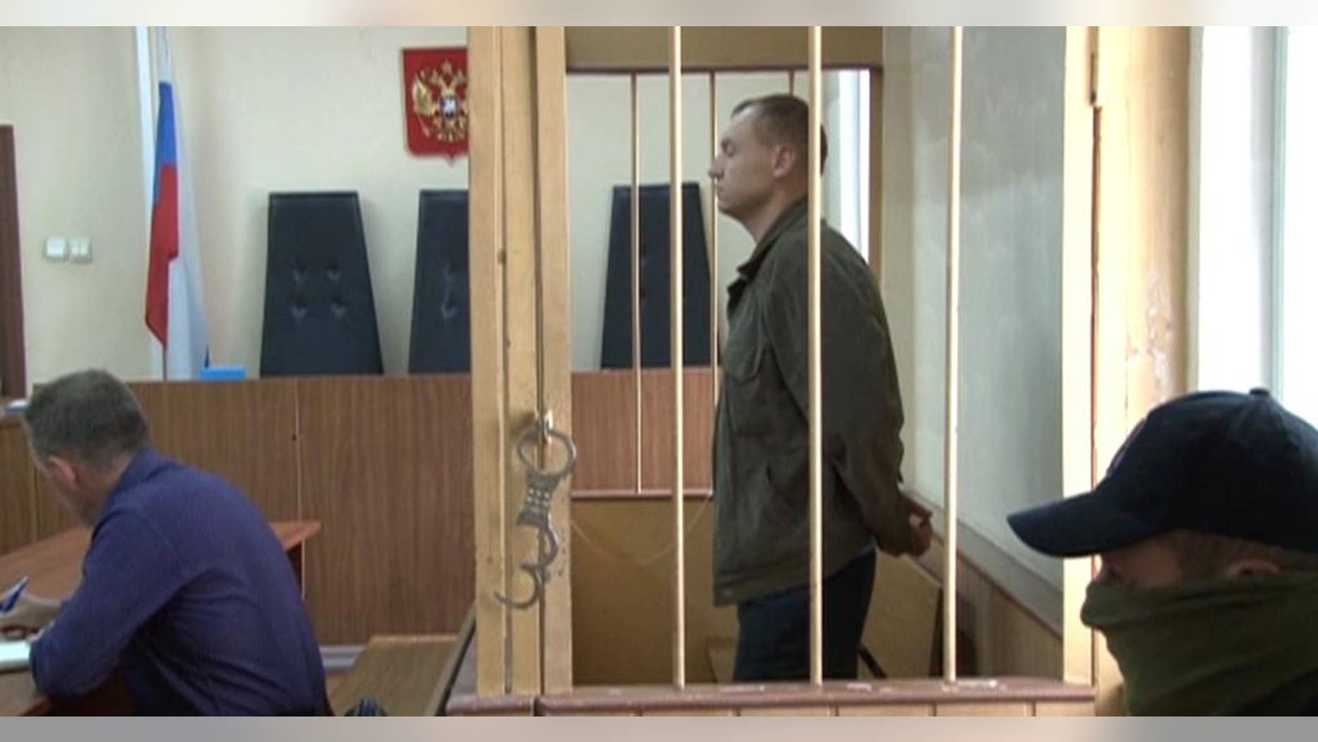 In this September 17, 2014 video grab made available by the APTN on Wednesday, Aug. 19, 2015 Eston Kohver of Estonia stands behind bars in Pskov, Russia. The regional court in the western city of Pskov on Wednesday, Aug. 19, 2015, found Kohver guilty of spying, arms smuggling and violating border regulations and ruled to send him to a high-security prison for 15 years. (AP Photo/APTN) TV OUT RUSSIA OUT