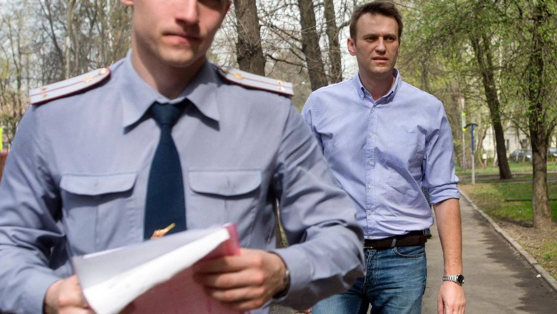 Russian opposition activist and anti-corruption crusader Alexei Navalny, right, is escorted to a court by a policeman, left, from his home, where he is currently staying under house arrest in Moscow, Russia, Tuesday, April 22, 2014. Russian opposition leader and anti-corruption crusader Alexei Navalny was found guilty in a libel case and fined US$8,400 in a court ruling that left the door open for his subsequent jailing. (AP Photo/Pavel Golovkin)