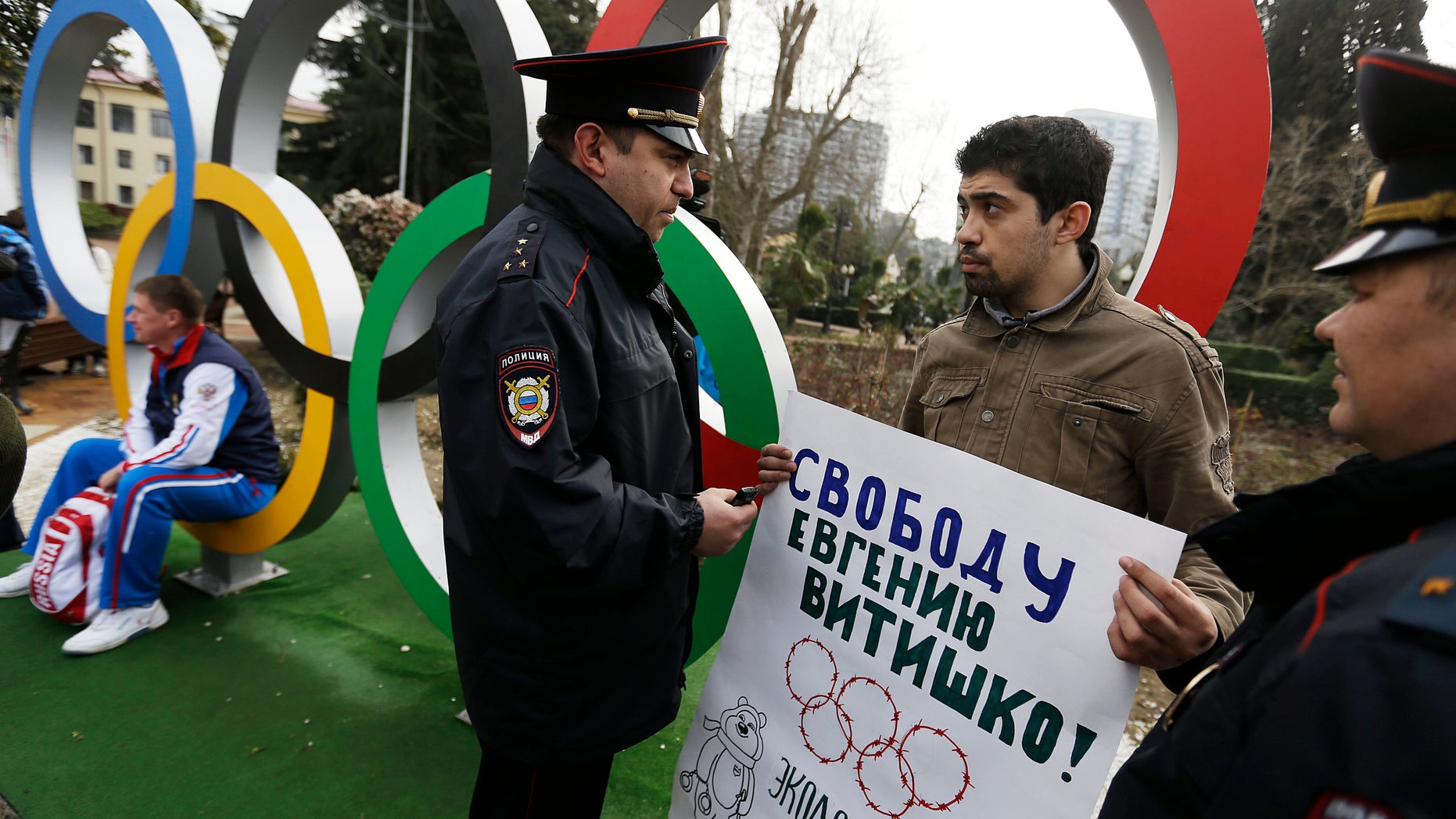 In this Monday Feb. 17, 2014 file photo, activist David Khakim, second right, is approached by two police officers after pulling out a banner protesting a recent prison sentence for a local environmentalist in front of the Olympic rings, in central Sochi, Russia. (AP Photo/David Goldman, file)