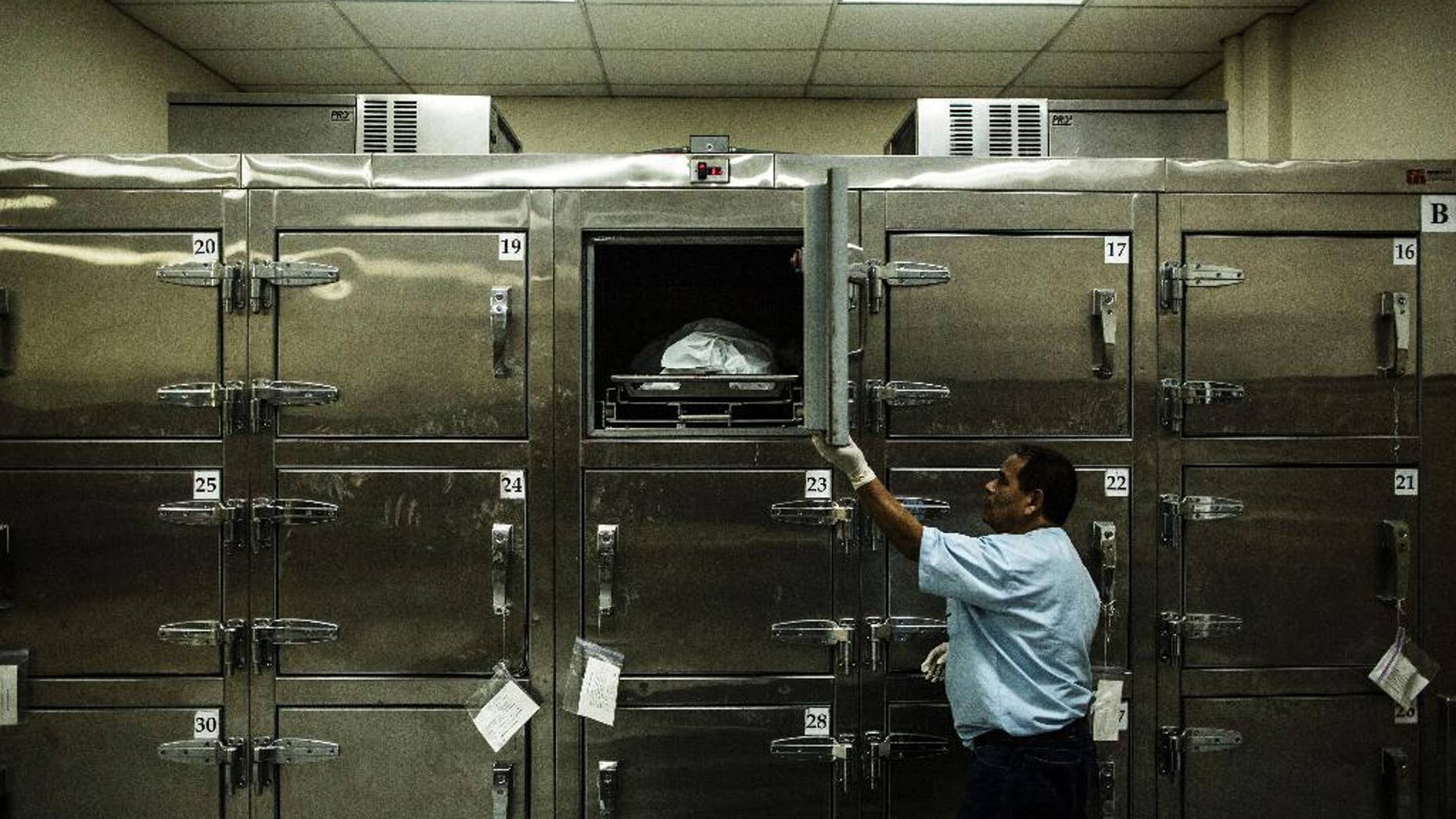 FILE - In this May 26, 2015 file photo, a forensic worker closes a morgue refrigerator door after placing a suspected gang member's body inside at the Institute of Legal Medicine in San Salvador, El Salvador. Authorities said on Wednesday, Aug. 19, 2015 that at least 125 people have been killed in the last three days as a wave of violence continues to plague the Central American nation. (AP Photo/Manu Brabo, File)