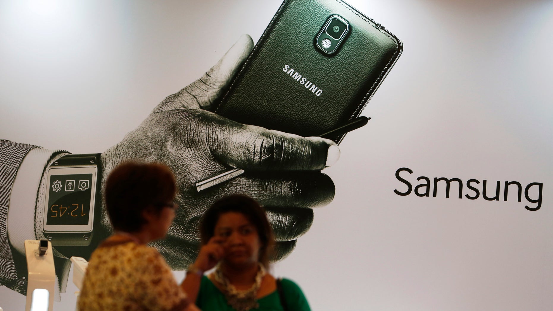 Women stand in front of an ad during the launch of the Samsung Galaxy Note 3 and Galaxy Gear in Jakarta, September 26, 2013.