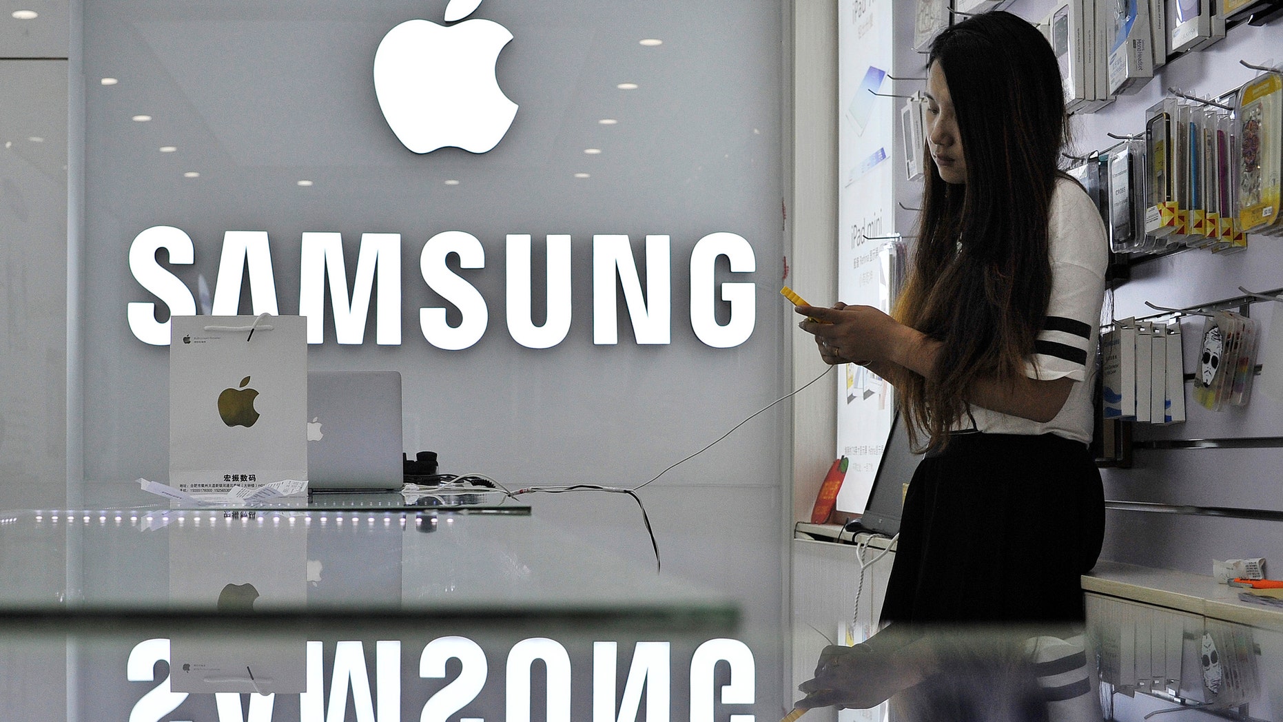 A sales assistant uses her mobile phone next to the company logos of Apple and Samsung at a store in Hefei, Anhui province September 10, 2014.
