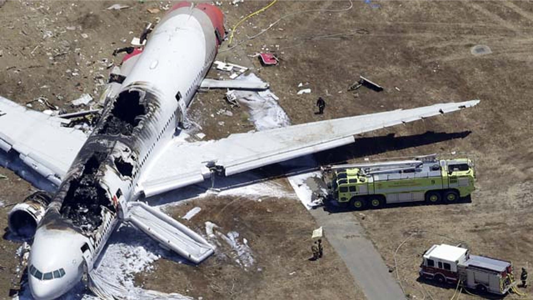 July 6, 2013: Firefighters, lower center, stand by a tarpaulin sheet covering the body of a Chinese teen struck by a fire truck during the emergency response to the crash of Asiana Flight 214 at the San Francisco International Airport in San Francisco. (AP Photo/Marcio Jose Sanchez)
