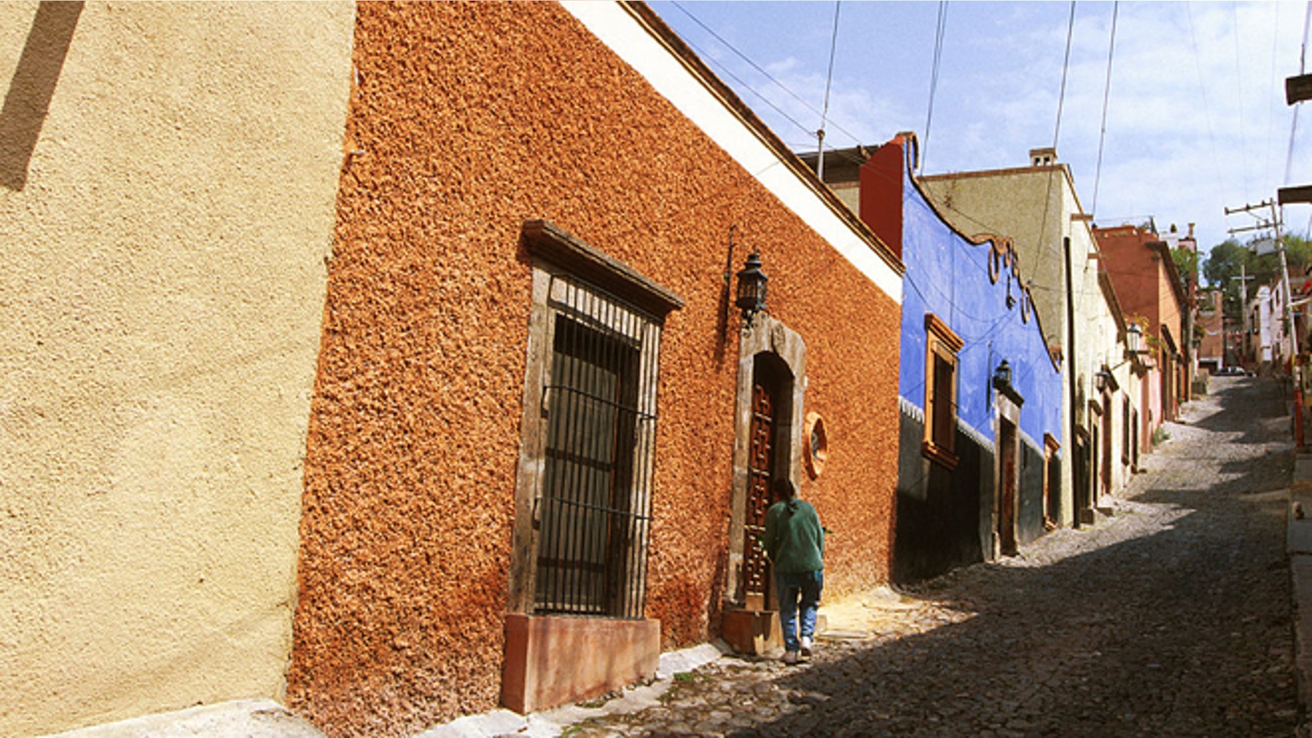 Mexico, San Miguel De Allende, Person Standing In Front Of A Doorway On A Cobblestone Roadway. (Photo by Education Images/UIG via Getty Images)