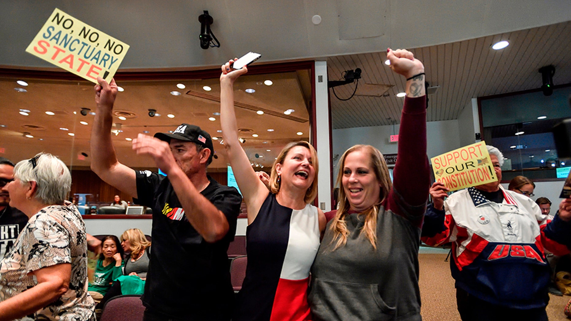 David Hernandez, left, Genevieve Peters, center, and Jennifer Martinez celebrate after the Orange County Board of Supervisors voted to join the U.S. Department of Justice lawsuit against the State of California's sanctuary cities law, March 27, 2018.