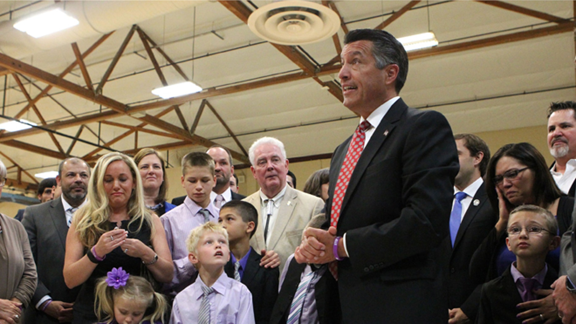 Surrounded by state lawmakers and the families of students who were victims of bullying, Nevada Gov. Brian Sandoval signs an anti-bullying bill into law at Carson Middle School in Carson City, Nev., Wednesday, May 20, 2015. (AP Photo/Cathleen Allison)