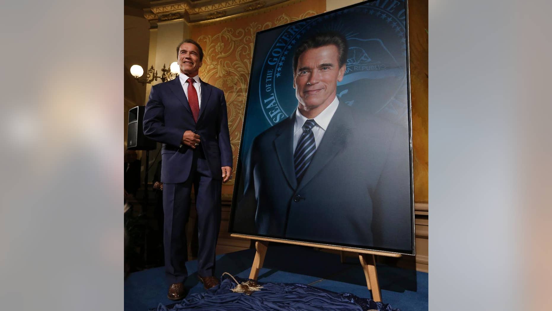 Former Gov. Arnold Schwarzenegger poses with his official portrait after it was unveiled at the Capitol in Sacramento, Calif., Monday, Sept. 8, 2014. The photograph-like giant image of the former governor was done by Austrian artist Gottfried Helnwein and will hang on the third floor of the Capitol. (AP Photo/Rich Pedroncelli)