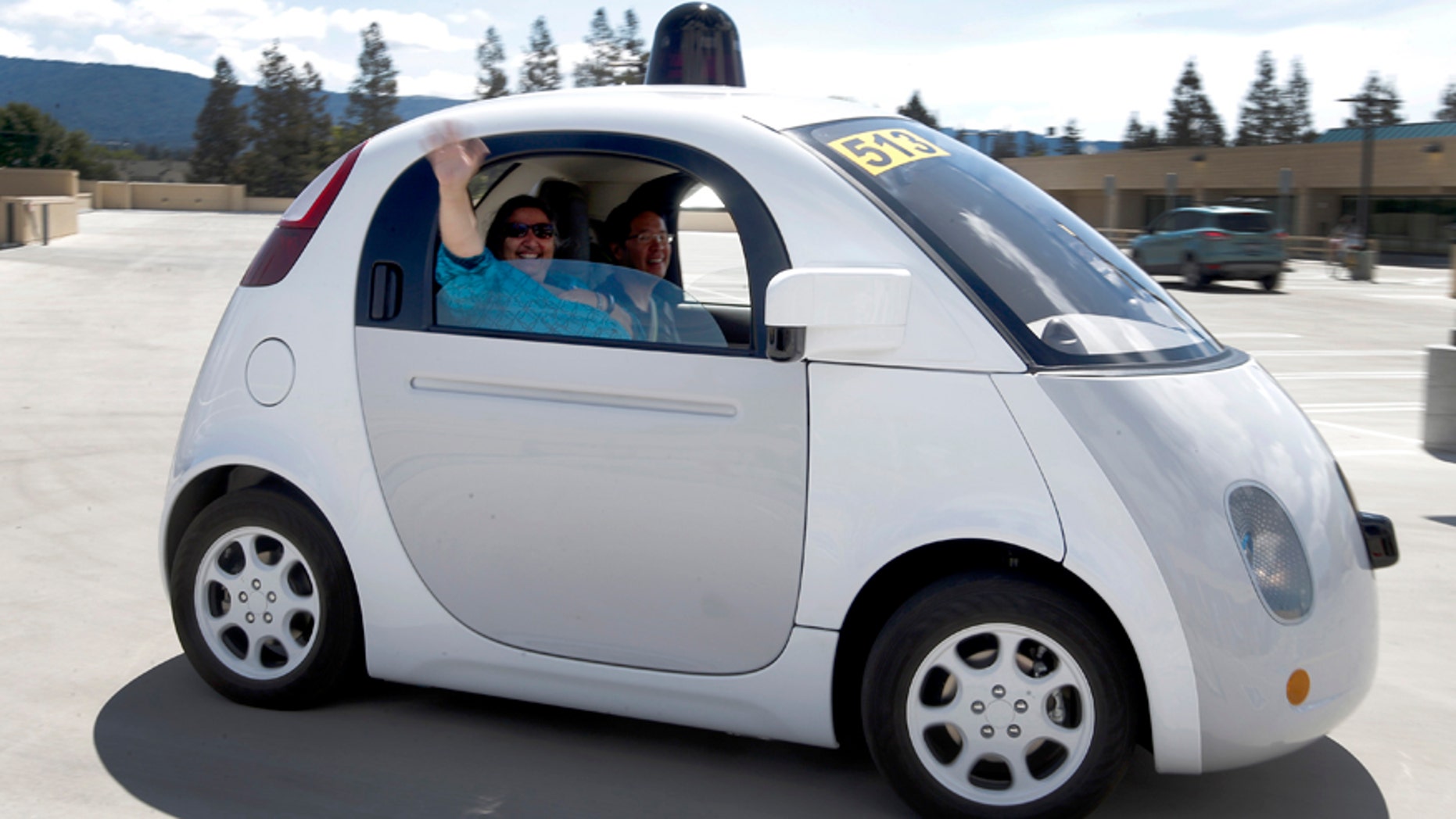 In this May 13, 2015 photo, Teresa Favuzzi, of Sacramento, waves as she gets a ride in the new Google self-driving prototype car during a demonstration at Google's campus in Mountain View, Calif. The plan of traditional automakers is to gradually automate more functions of driving until, perhaps by 2025, some cars will be fully capable of driving themselves. But Google, Alibaba, Baidu and other tech companies are aggressively working on their own self-driving vehicles, and could leapfrog the car industry in bringing them to market. (AP Photo/Tony Avelar)