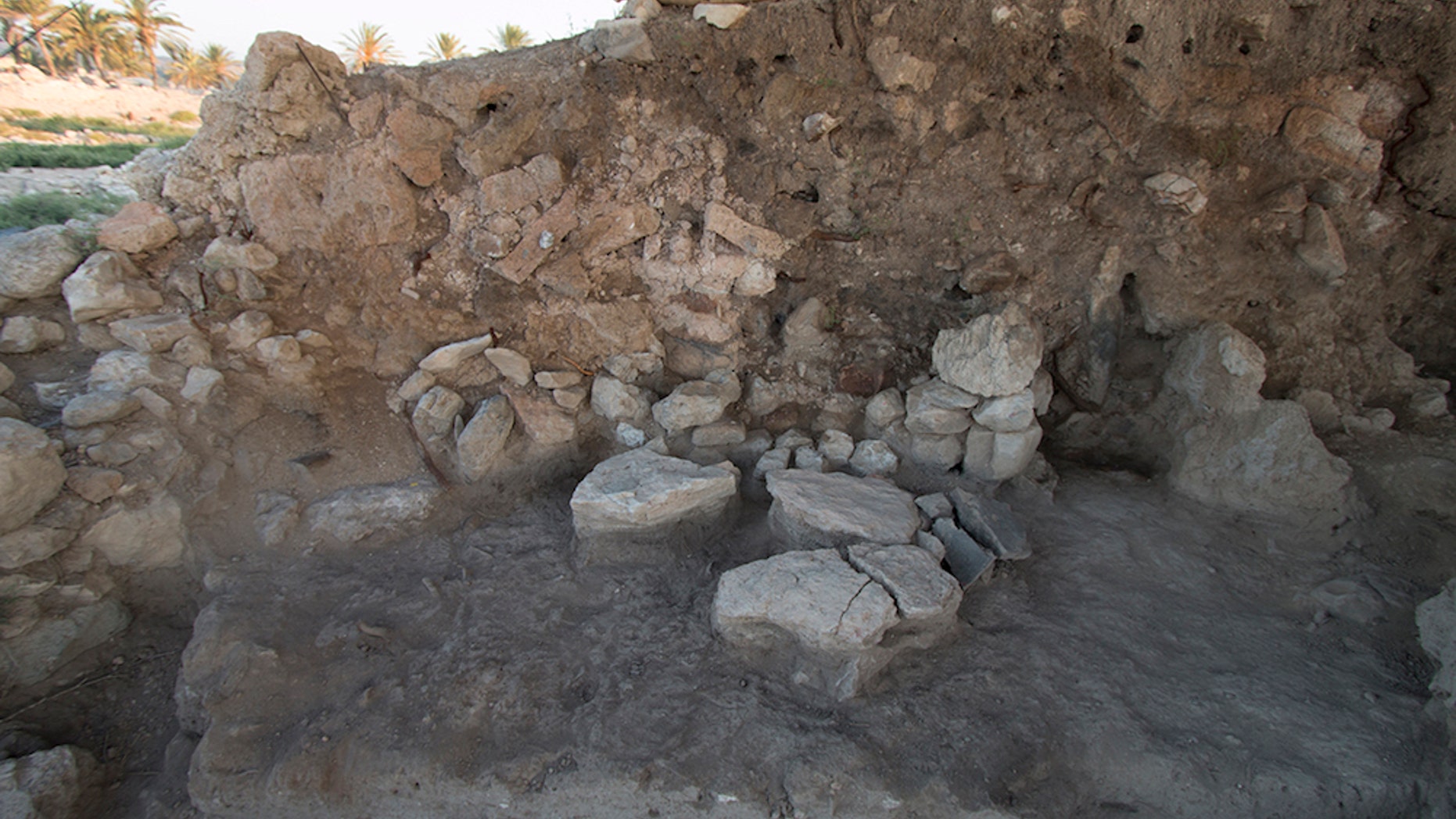 An excavated area at Tel Megiddo from 2014 shows a stone-paved floor that has fire-blackened sediment. The wall consists of collapsed red and yellowish mud bricks.