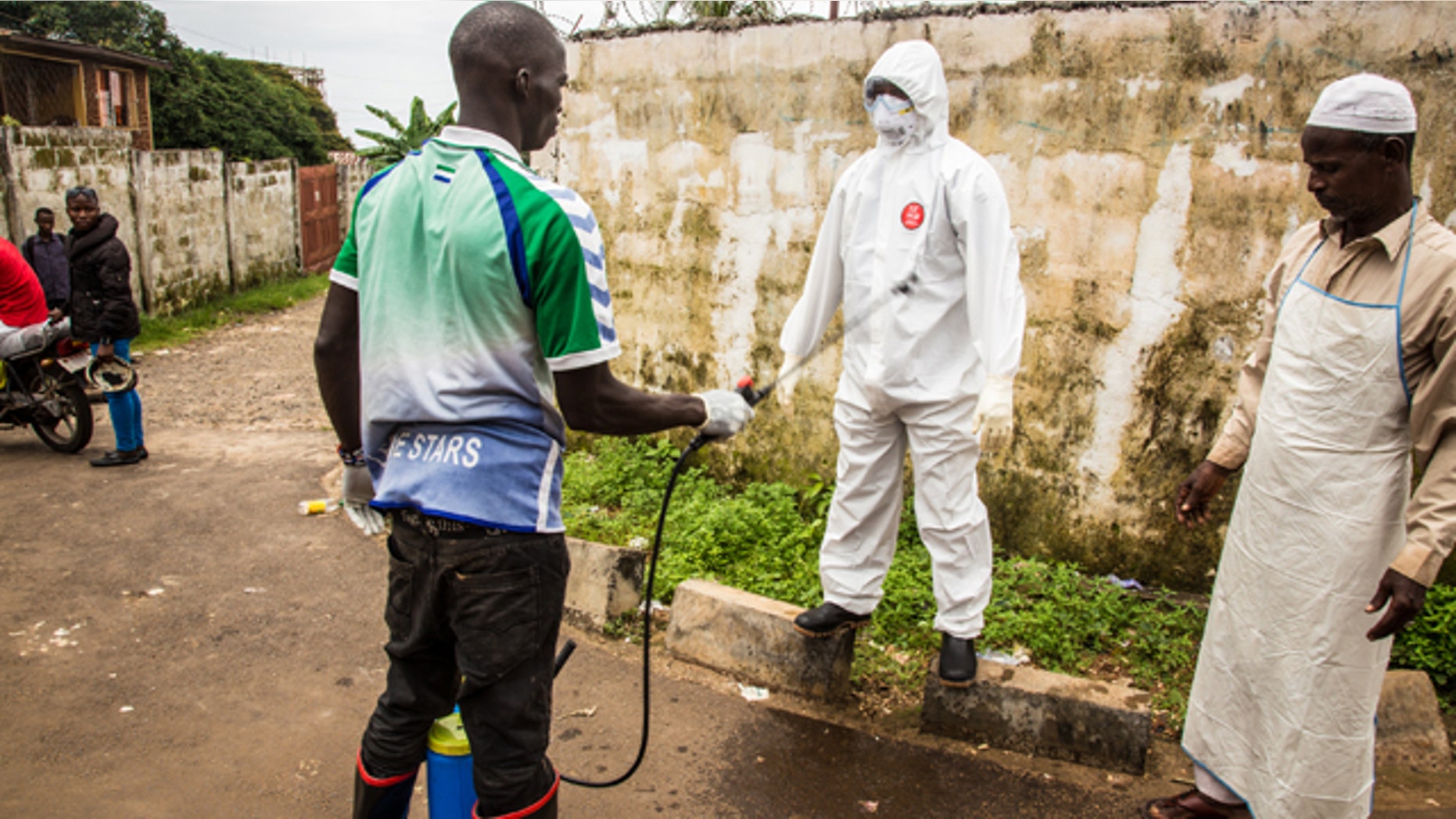 September 24, 2014: A health worker sprays disinfectant on a colleague after he assisted in the loading of a man suspected of suffering from the Ebola virus into an ambulance, in Freetown, Sierra Leone. (AP Photo/ Michael Duff)