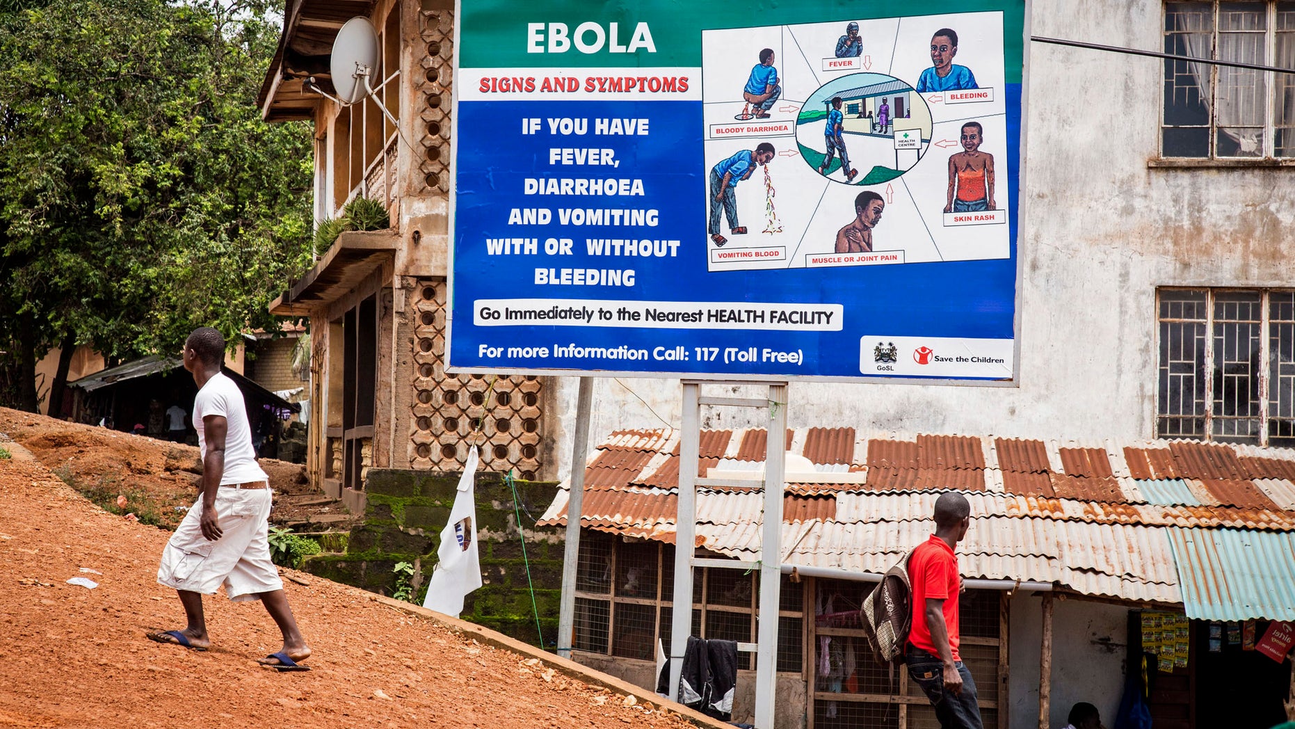 People walk past a billboard encouraging people suffering from symptoms linked to Ebola to present themselves at a health facility for treatment in Freetown, Sierra Leone, AP Photo