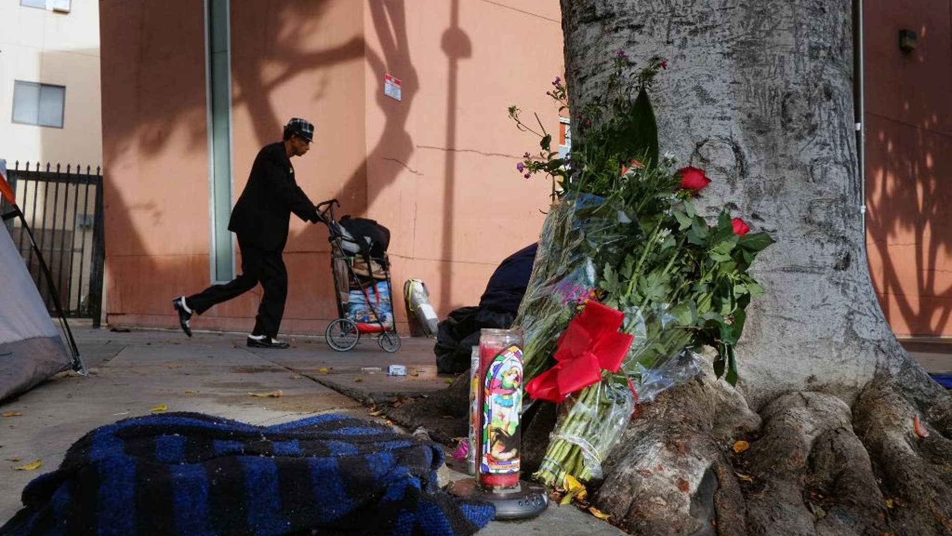 FILE - This March 2, 2015 file photo shows a pedestrian walks past flowers and candles placed on a sidewalk near where Charly Keunang a homeless man was shot and killed by police in the Skid Row section of downtown Los Angeles. An officer dropped a nightstick during the struggle with Keunang and the woman who picked it up now faces an assault charge that could send her to prison for 25 years to life. The March shooting was captured on video, which shows Trishawn Cardessa Carey, 34, briefly lifting the baton as police scuffled with Keunang. (AP Photo/Richard Vogel,File)