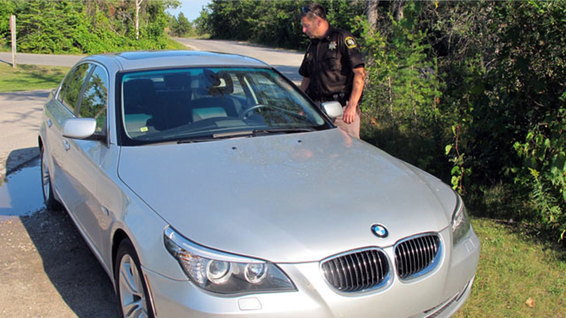 August 26, 2013: Mike Borkovich, sheriff of Leelanau County, Mich., examines a car parked at Sleeping Bear Dunes National Lakeshore that is believed to have been used by a missing man and his three children. The man, who is wanted on a domestic violence charge, and his children have been found safe. (AP Photo)