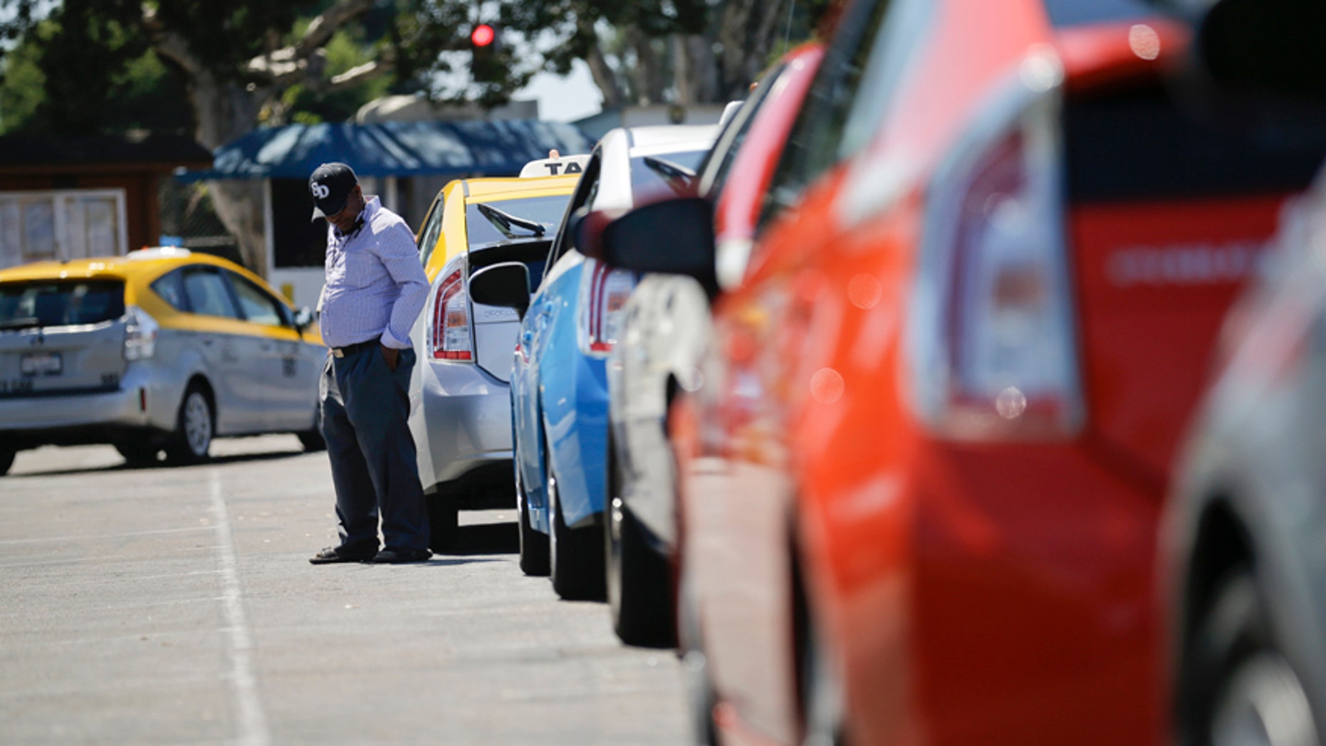 A cab driver waits near his car in line at a depot near the airport Wednesday, Sept. 10, 2014, in San Diego. Airport inspectors are judging how taxi drivers smell, a practice that some drivers say may lead to discrimination against immigrants. (AP Photo/Gregory Bull)