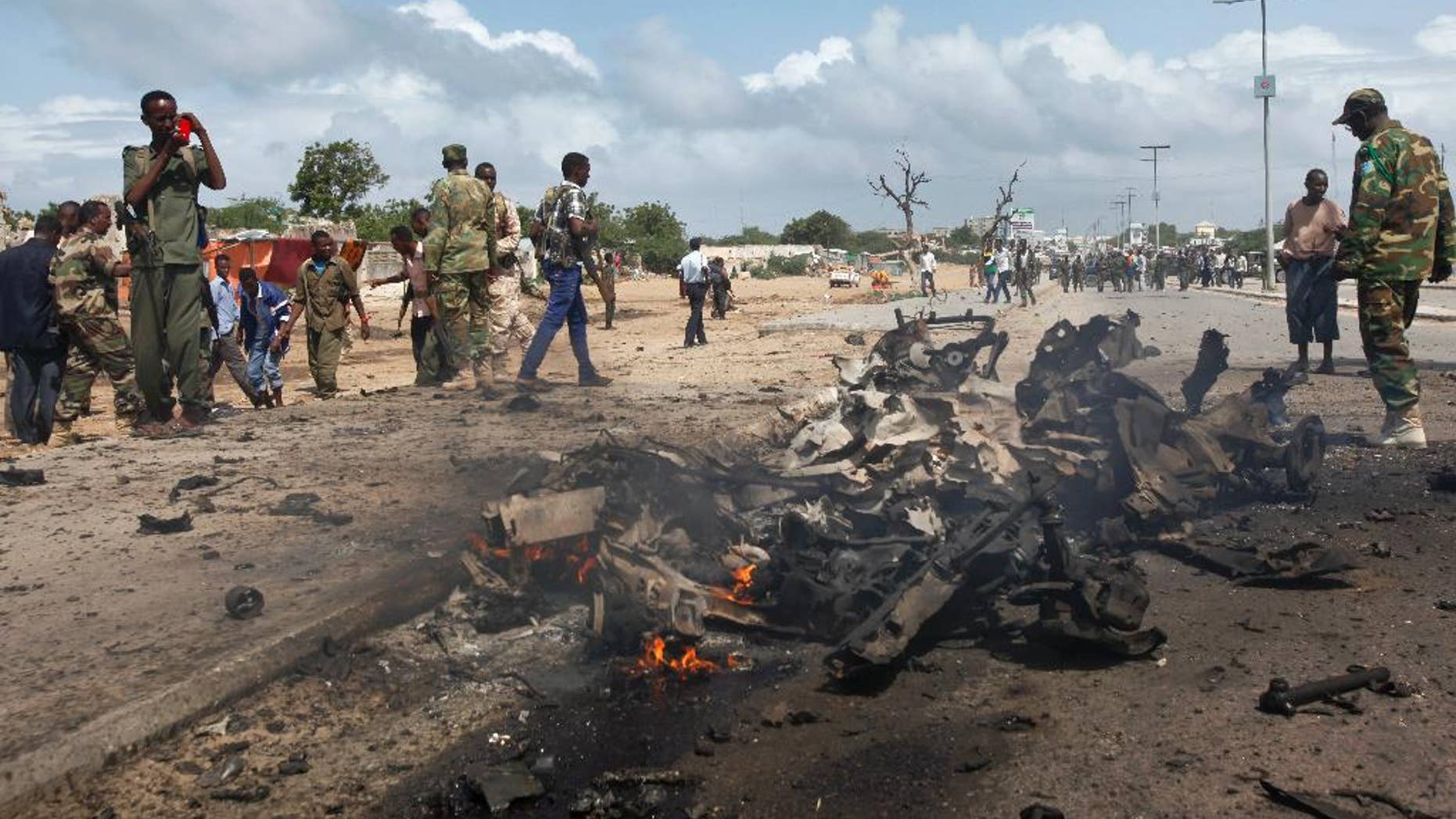 Somali soldiers stand near the wreckage at the scene of a suicide car bomb attack which targeted a convoy of foreign officials, in Mogadishu, Somalia Wednesday, June 24, 2015. (AP Photo)