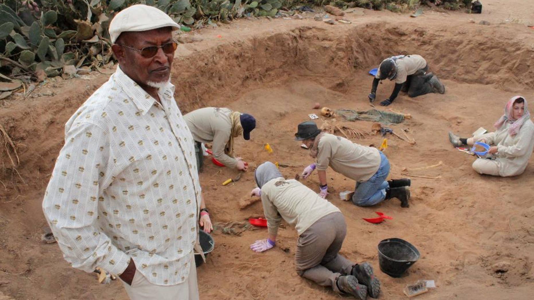 In this photo taken Tuesday, Feb. 18, 2014, Chairman of the Somaliland War Crimes Commission Kadar Ahmed, left, oversees members of the Peruvian Forensic Anthropology Team as they work to uncover bodies buried in a mass grave in Hargeisa, Somaliland, a breakaway region of Somalia. An American volunteer gently brushes away dirt to reveal the bones of a Somali victim buried in a mass grave some 30 years ago. Tens of thousands of skeletons may lie in mass graves here, on the northern edge of Somalia, where many want to see justice prevail, even if delayed. Last year 38 bodies were uncovered in two graves by the Somaliland War Crimes Investigation Commission, which is overseeing the work on a third site where another dozen bodies are buried. (AP Photo/Jason Straziuso)