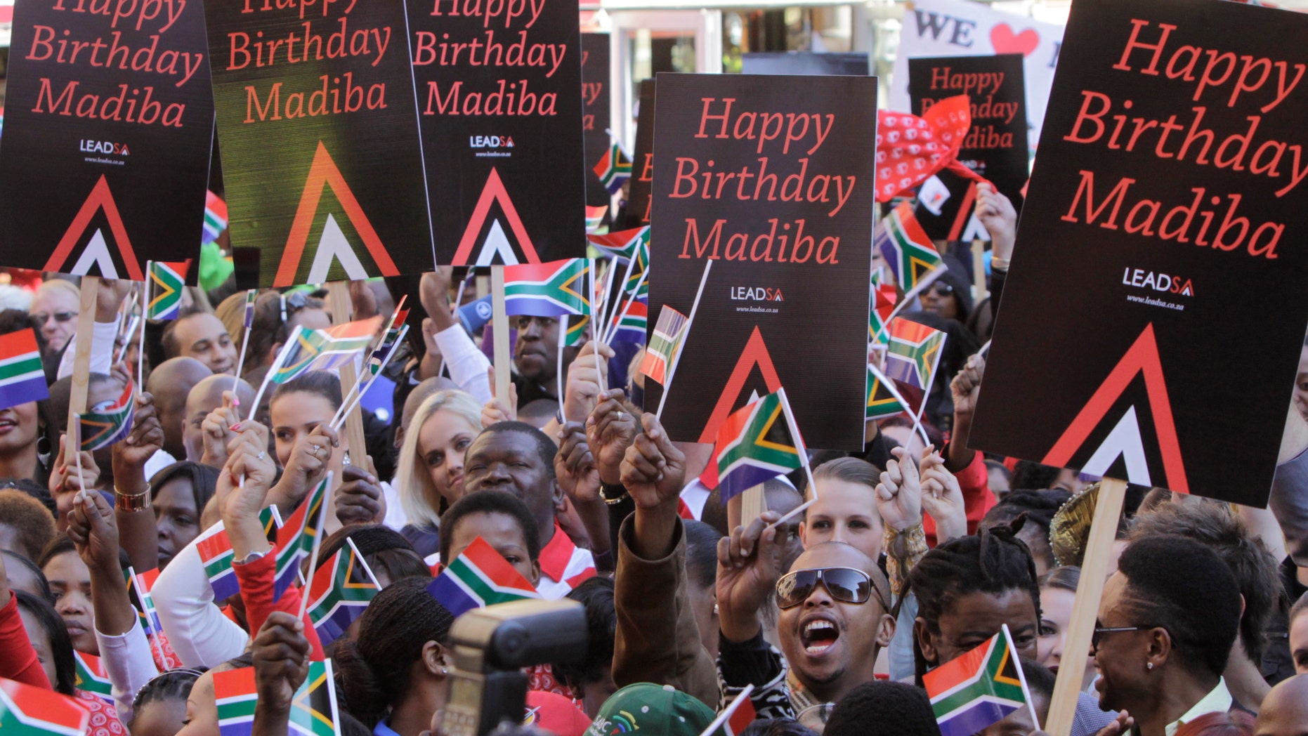 In this photo taken Friday June 1, 2012, members of the public and celebrities gather to videotape a sing-a-long birthday wish for former president Nelson Mandela, portrait on woman's shirt, on Nelson Mandela Square in Johannesburg. Mandela's office on Monday June 18 2012 has released the video of South Africans singing "Happy Birthday" in an effort to motivate people around the world to salute the anti-apartheid icon ahead of his 94th birthday next month. (AP Photo/Denis Farrell)