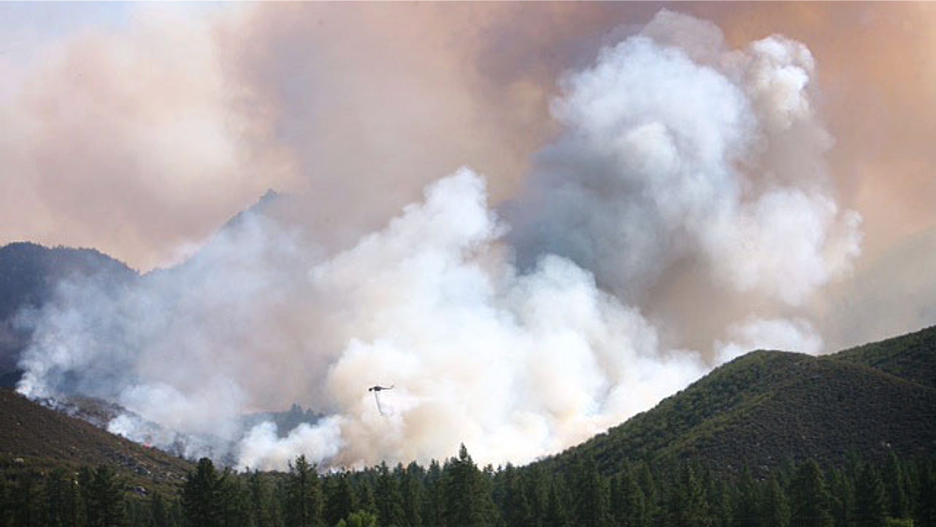 July 16, 2013: A water-dropping helicopter is dwarfed by the smoke rising from the Mountain Fire wildfire burning near Mountain Center, Calif. A fast-moving wildfire in the mountains west of Palm Springs nearly doubled in size Tuesday, prompting the evacuation of about 50 homes. (AP Photo/The Press-Enterprise,Kurt Miller )