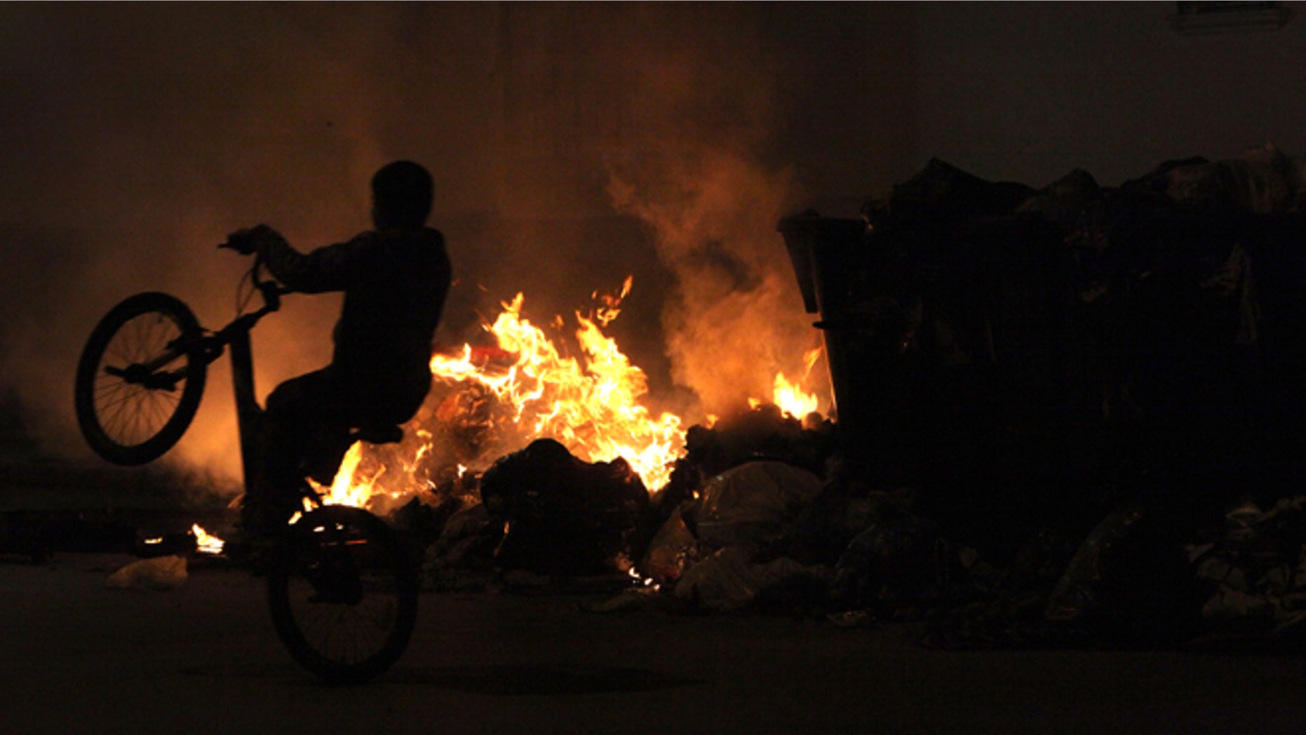 A boy rides his bicycle next to burning garbage piled up in the middle of the street in Jerez de la Frontera, Cadiz province in Andalucia, southern Spain Wednesday, Nov. 21, 2012. A garbage strike has been ongoing now for nineteen days and has resulted in more than 3,000 tons of garbage piled up on the streets and the burning of rubbish containers by local residents. (AP Photo/Javier Fergo)