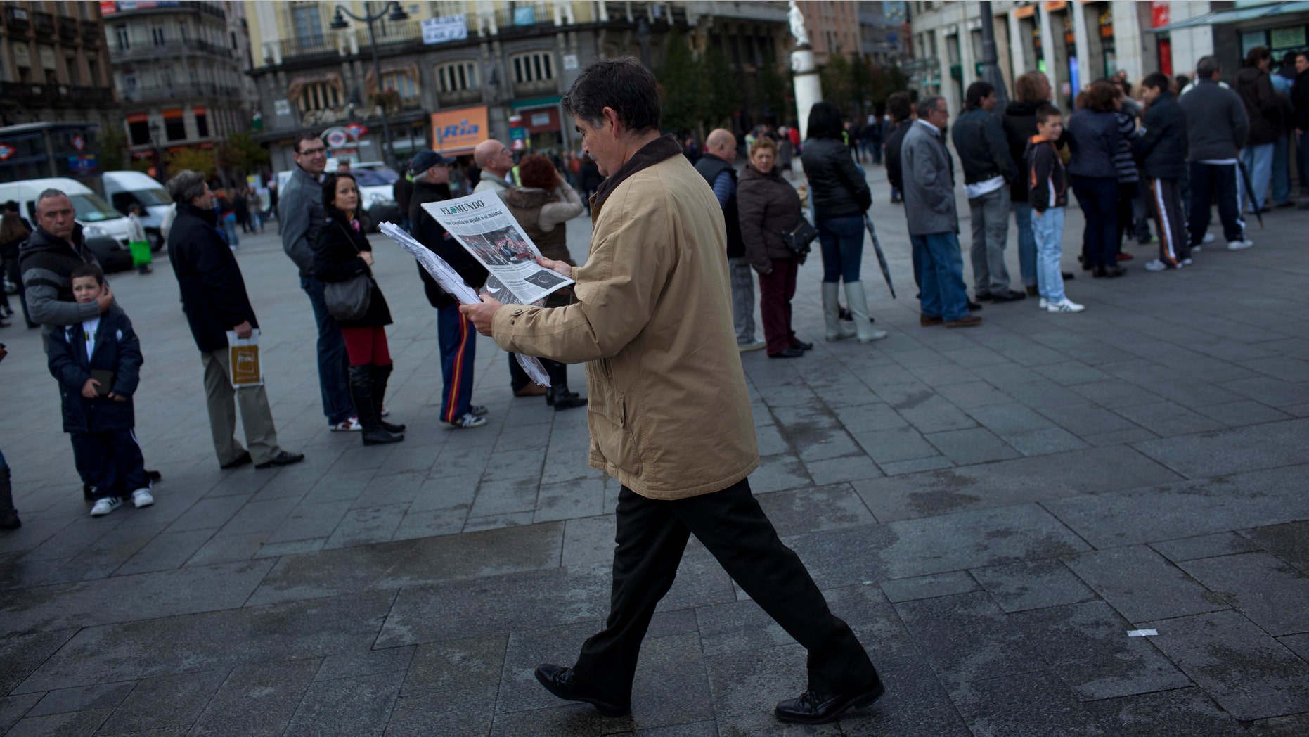 A man reads the news about the Spanish electoral campaign as others line up waiting to buy lottery in Madrid, Spain, Saturday, Nov. 19, 2011. Spain will hold general elections on Nov. 20. (AP Photo/Emilio Morenatti)
