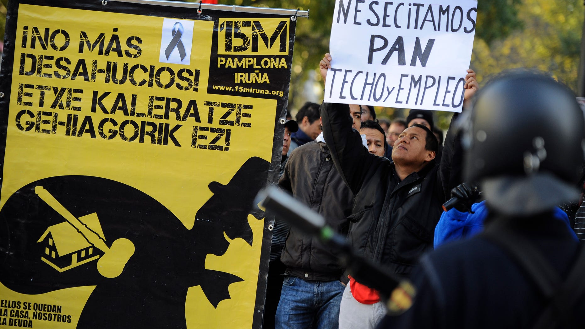 Nov. 14, 2012: A man who identified himself as Edwin, 32, from Ecuador, right, who was evicted from his home over debts, holds up banner reading ''We need bread, roof and employment'' beside a poster to support people fighting against evictions reading, ''No More Evictions'', in front of Spanish riot police during a general strike against government austerity measures, in Pamplona, northern Spain.