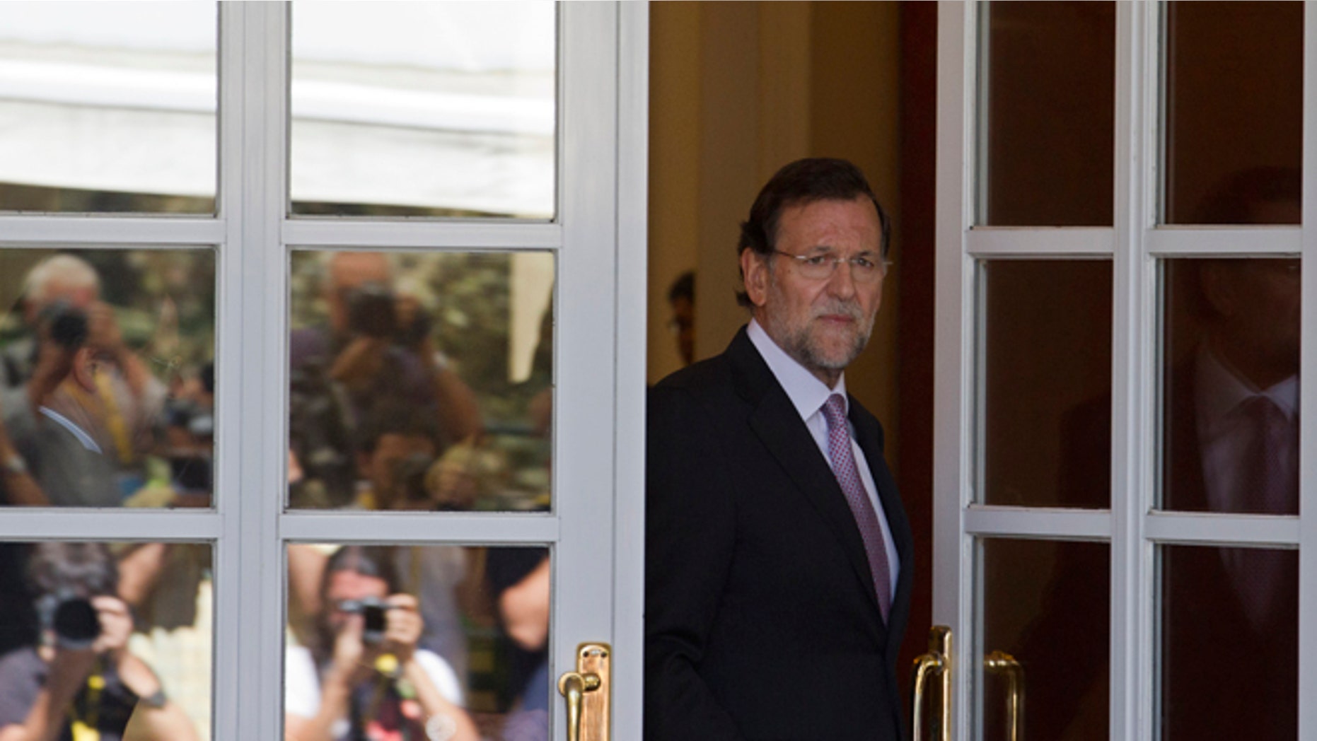 Photographers are seen reflected in a glass door as Spain's Prime Minister Mariano Rajoy steps out to greet European Council President Herman van Rompuy, unseen at the Moncloa Palace in Madrid Tuesday Aug. 28, 2012. Rajoy and van Rompuy met for talks on the economic crisis and Spain's battle to avert having to seek a sovereign bailout. (AP Photo/Paul White)