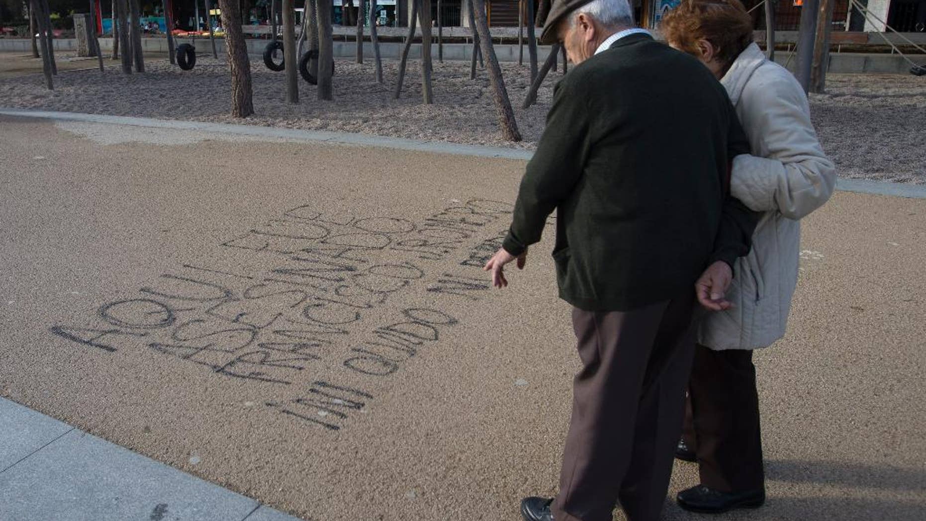 A couple stop to look at words painted on the ground by the Manzanarez river near where a 43-year-old Deportivo fan was killed, Madrid, Spain, Monday, Dec. 1, 2014. The man died and 11 others suffered minor injuries after a fight broke out across the river from Atletico de Madrid's soccer stadium between its fans and those of visiting team Deportivo La Coruna on Sunday. Madrid's Clinico San Carlos hospital said a man died of injuries sustained in the clash between rival fans that broke out hours before the game near the Vicente Calderon stadium and had to be removed from the river. Police made several arrests. Writing in Spanish reads: 'Here, Francisco J. Romero was murdered. I will never forget or Forgive' (AP Photo/Paul White)