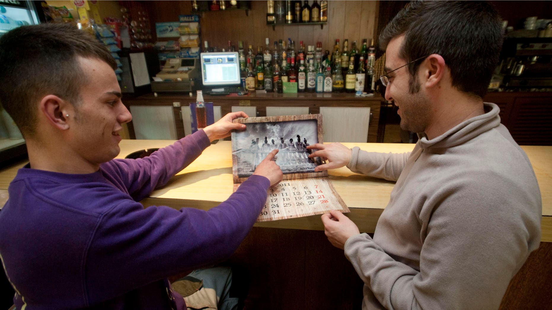 Pere Mestre, left, and Joan Bauza, right, pose pointing to their places in the calendar photo at a bar, in Sant Joan, Mallorca, Spain on Friday, Jan. 7, 2011. Seeking to raise money for their Roman Catholic youth group on the Spanish tourist destination island of Mallorca, members came up with a risque idea: Pose nearly nude for a calendar recreating scenes from the Passion of Christ. (AP Photo/Manu Mielniezuk)