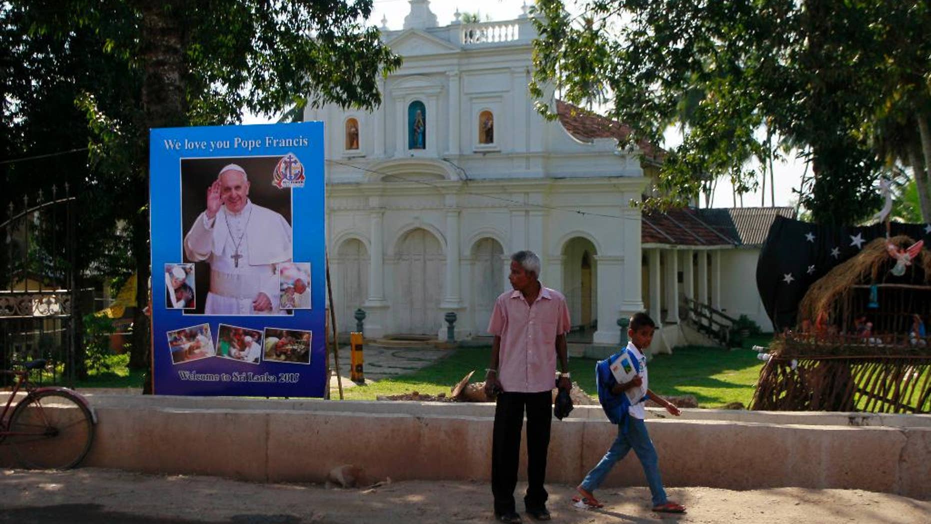 FILE - In this Tuesday, Jan. 6, 2015 file photo, Sri Lankans walk past a poster to welcome Pope Francis outside a church in Moratuwa, on the outskirts of Colombo, Sri Lanka. Less than a week after its longtime president was surprisingly voted out of office, Sri Lanka welcomes Pope Francis on Tuesday, with the island nation’s Catholic minority hoping he can help heal the lingering wounds of the country's 25-year civil war. (AP Photo/Eranga Jayawardena, File)