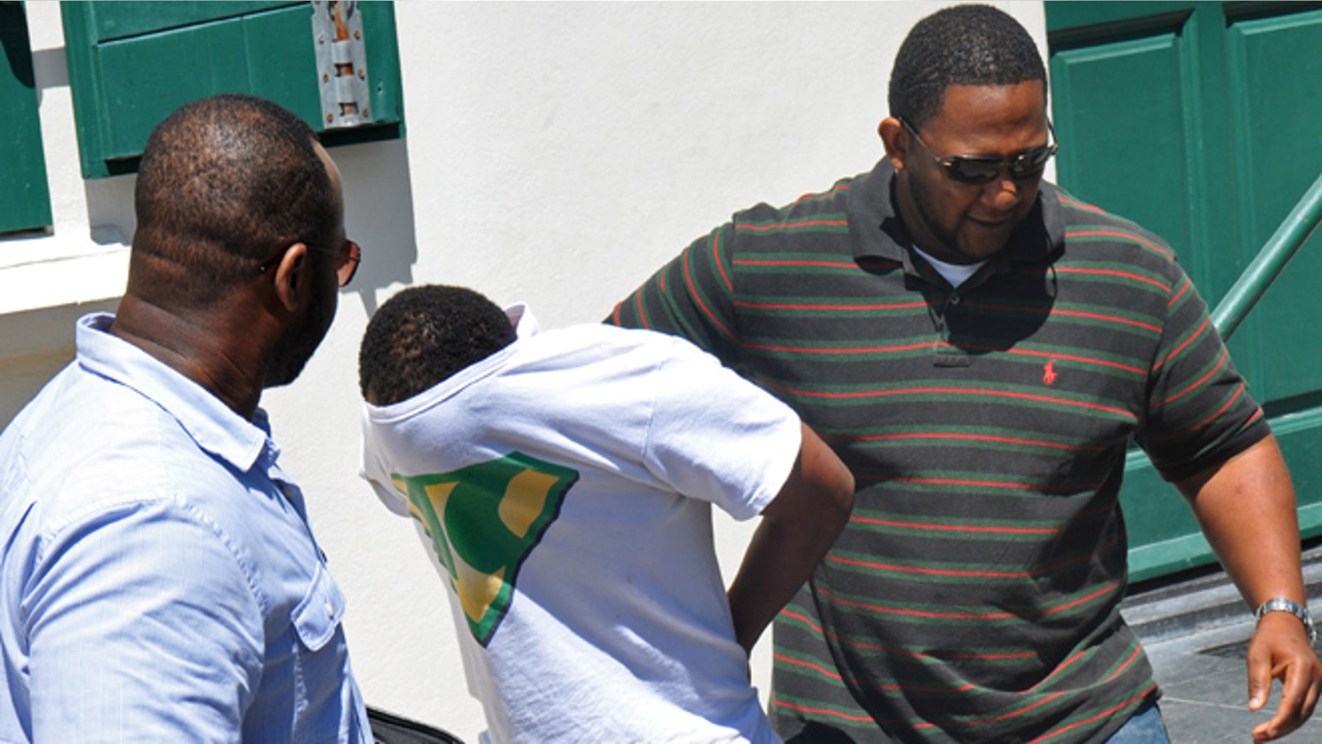 With his T-shirt pulled over his head, Jamaican Meyshane Johnson, center, a suspect in the slaying of a South Carolina couple, is escorted by police officers outside the court building after his arraignment in Philipsburg, St. Maarten.